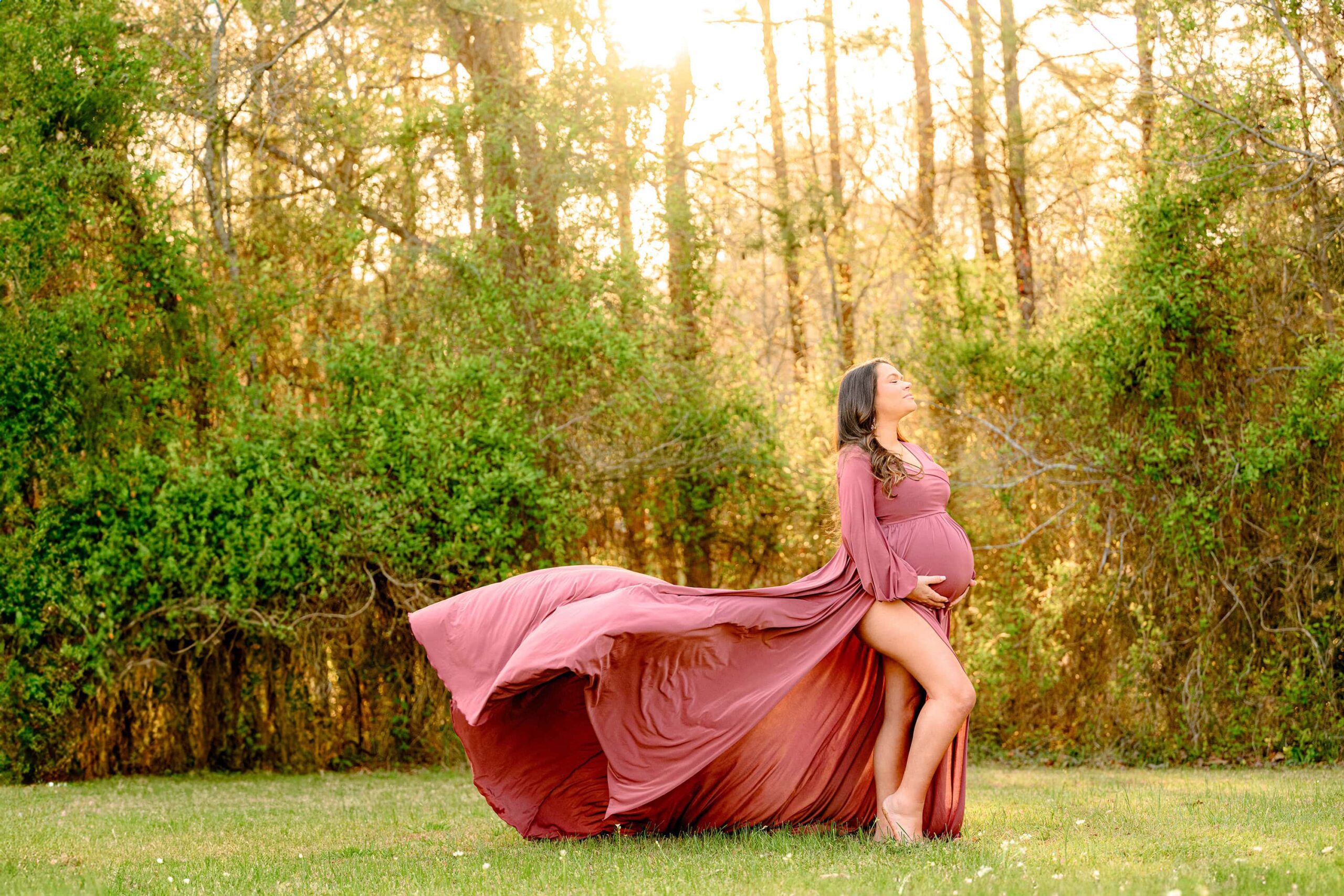 the train on the charlotte area expectant mother's rose pink dress is floating in the air while mom looks up at the sun glow