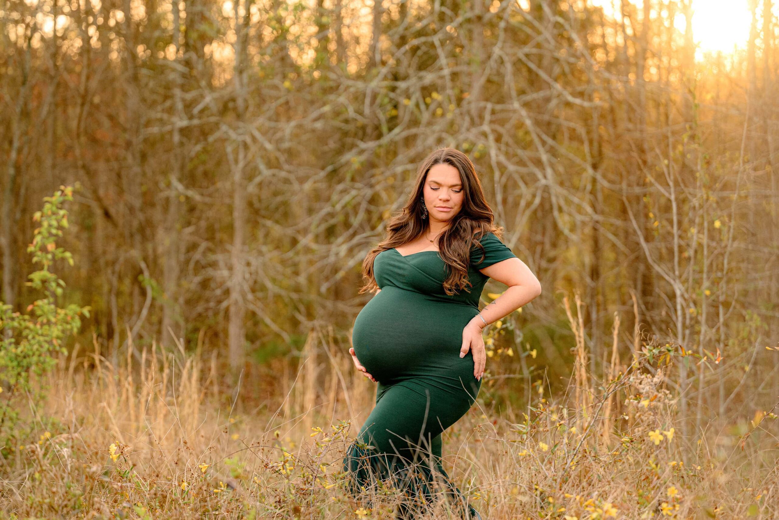 the golden sun glows down on a charlotte expectant mother dressed in hunter green during her maternity photoshoot in a waxhaw park