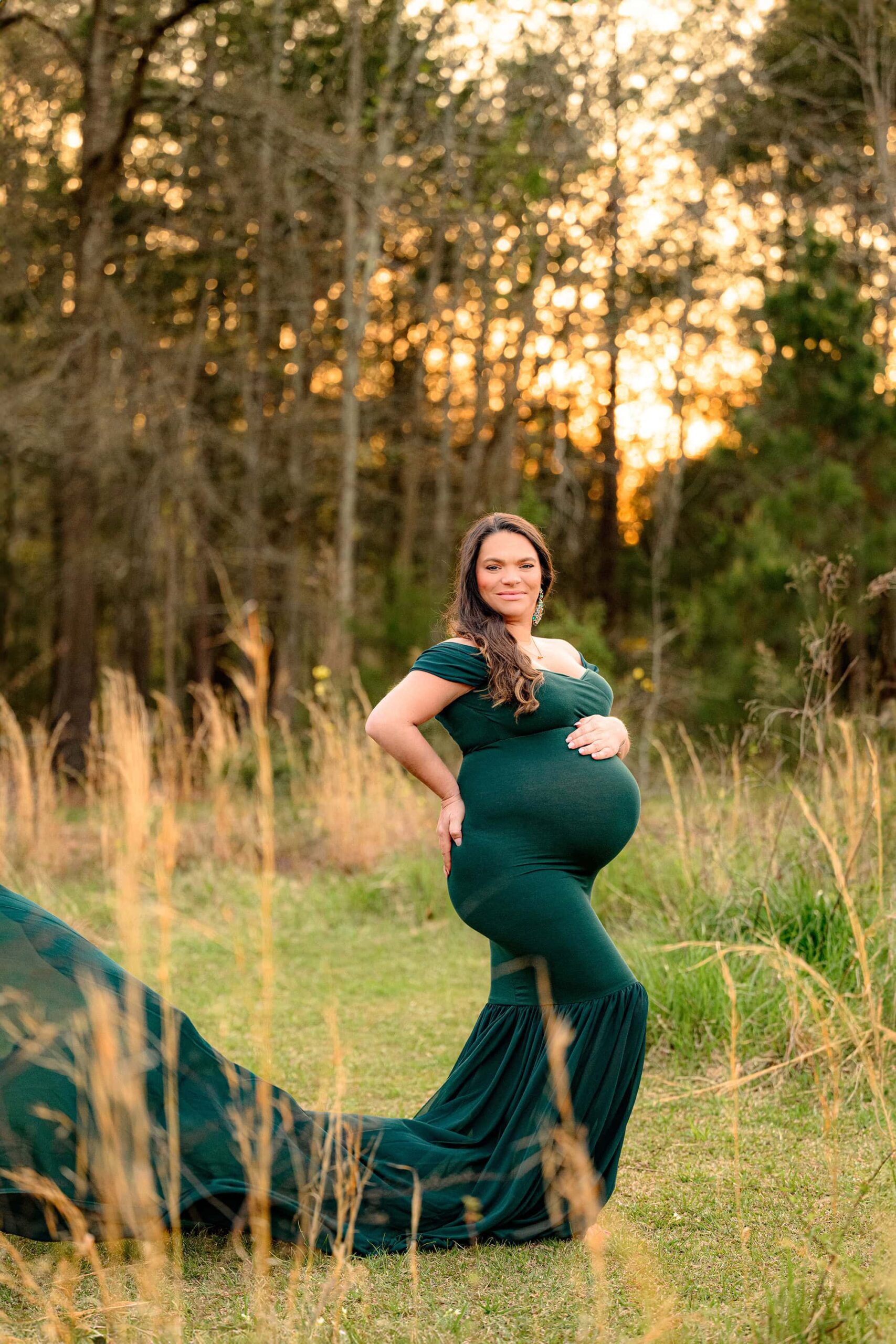 expectant mom poses in a waxhaw field during her spring maternity photoshoot wearing a mermaid hunter green dress