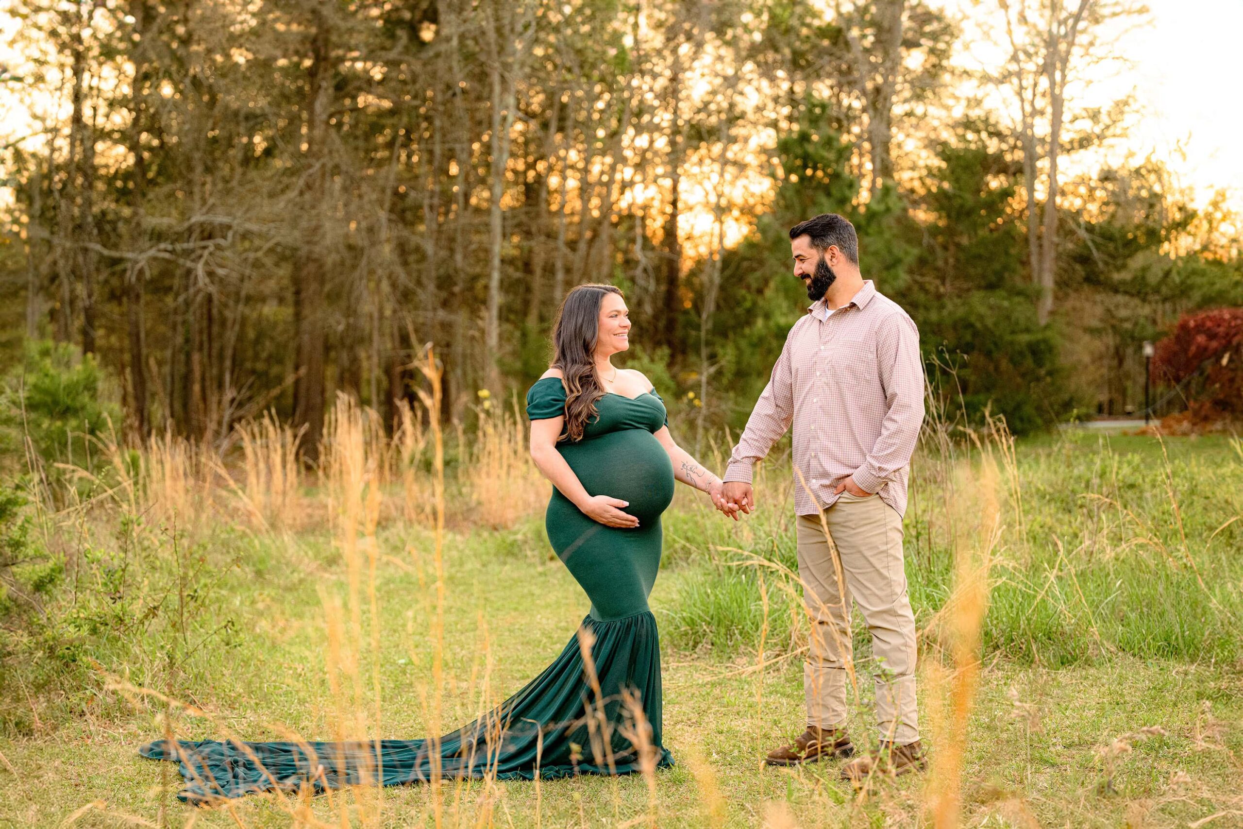 couple is hand in hand in a waxhaw park. mom is wearing a mermaid style hunter green dress and dad is in brown shirt and pants