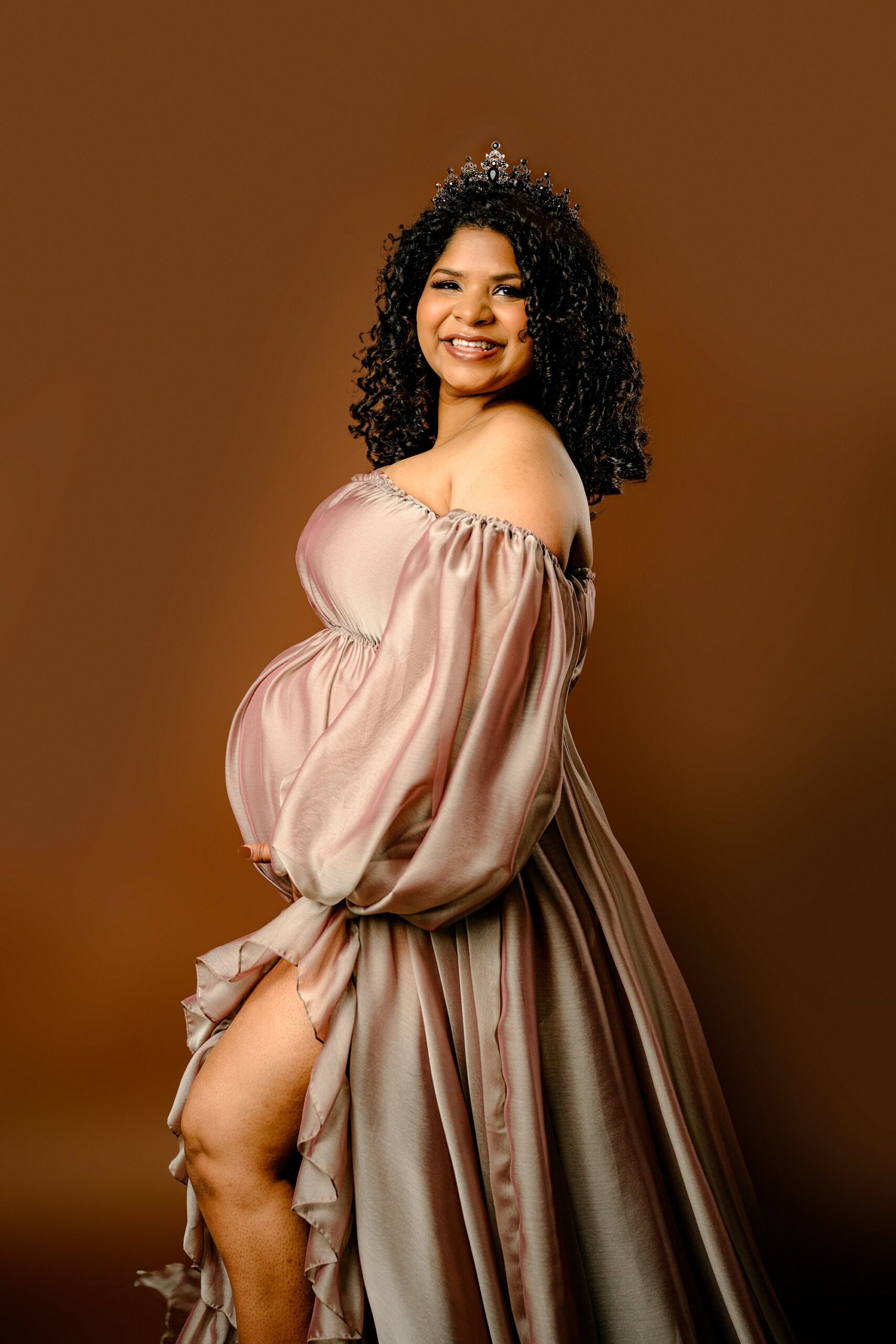 expectant mother cradles her baby bump during her maternity session. she is wearing a brown dress and crown
