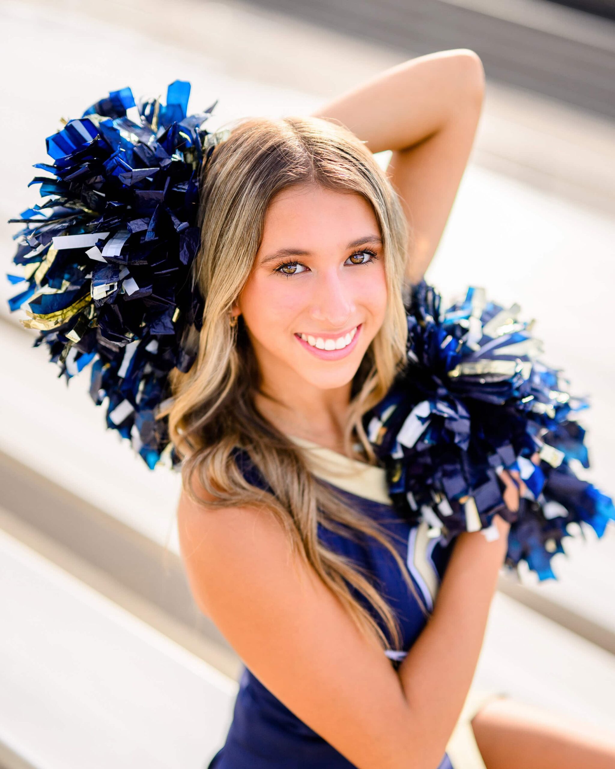 A cheerleader from Cuthbertson High School poses with her arms extended, holding a pom in each hand—one in front and one behind her—while smiling confidently.