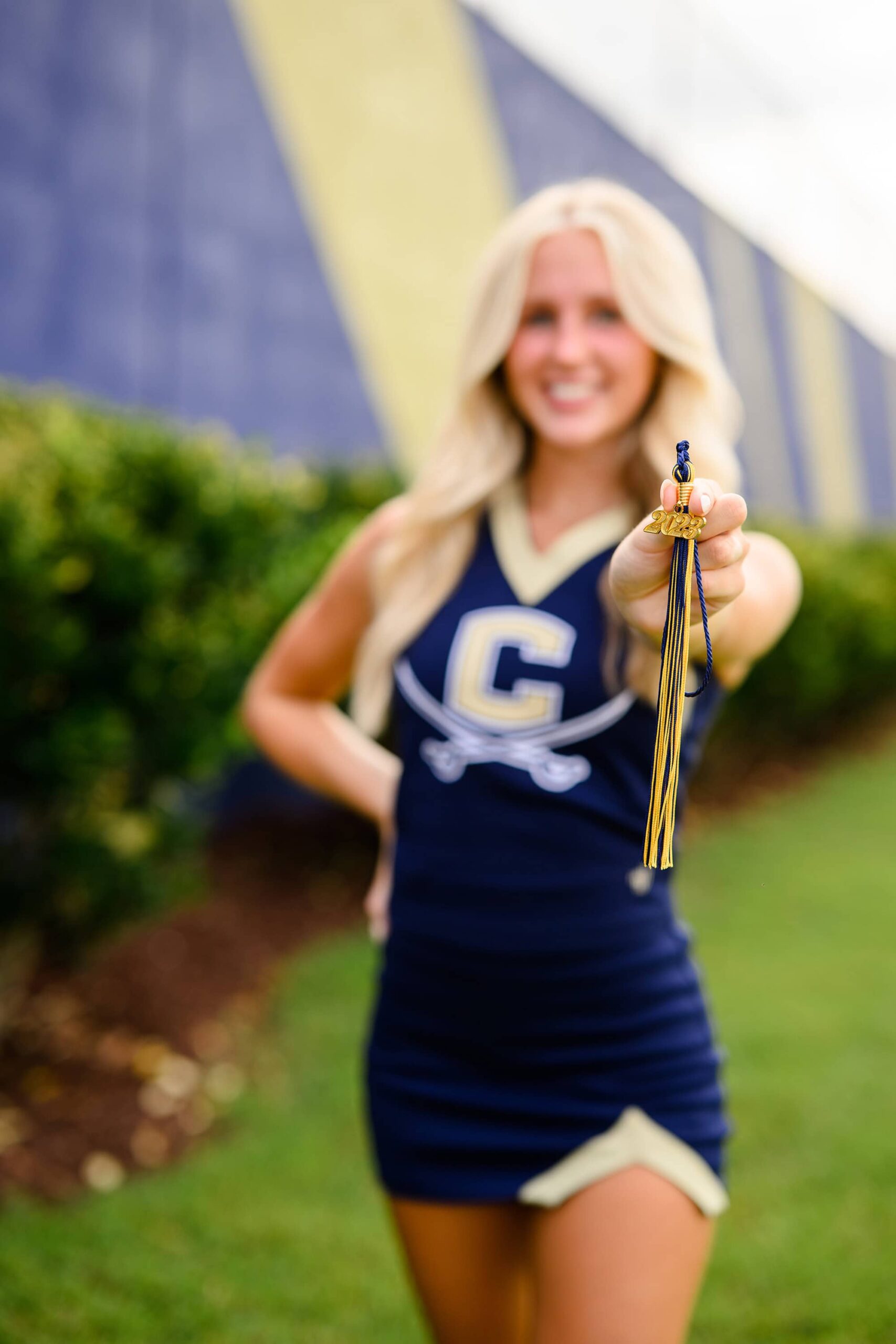 A blonde cheerleader from Cuthbertson High School proudly holds her graduation tassel while posing for her senior photo.