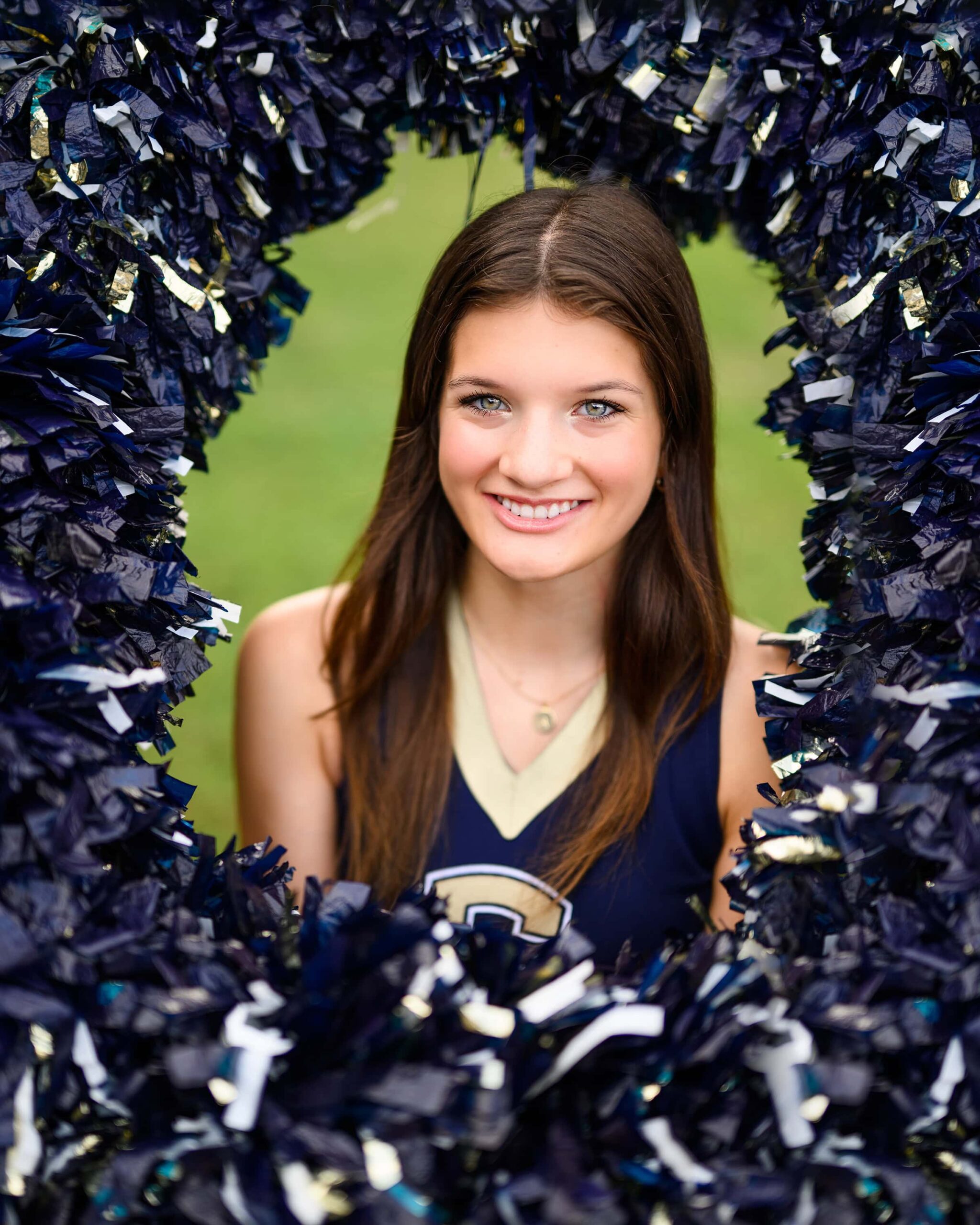 A dark-haired senior cheerleader from Cuthbertson High School is positioned in the middle of a pom-pom ring, her head surrounded by a circle of poms as she smiles.
