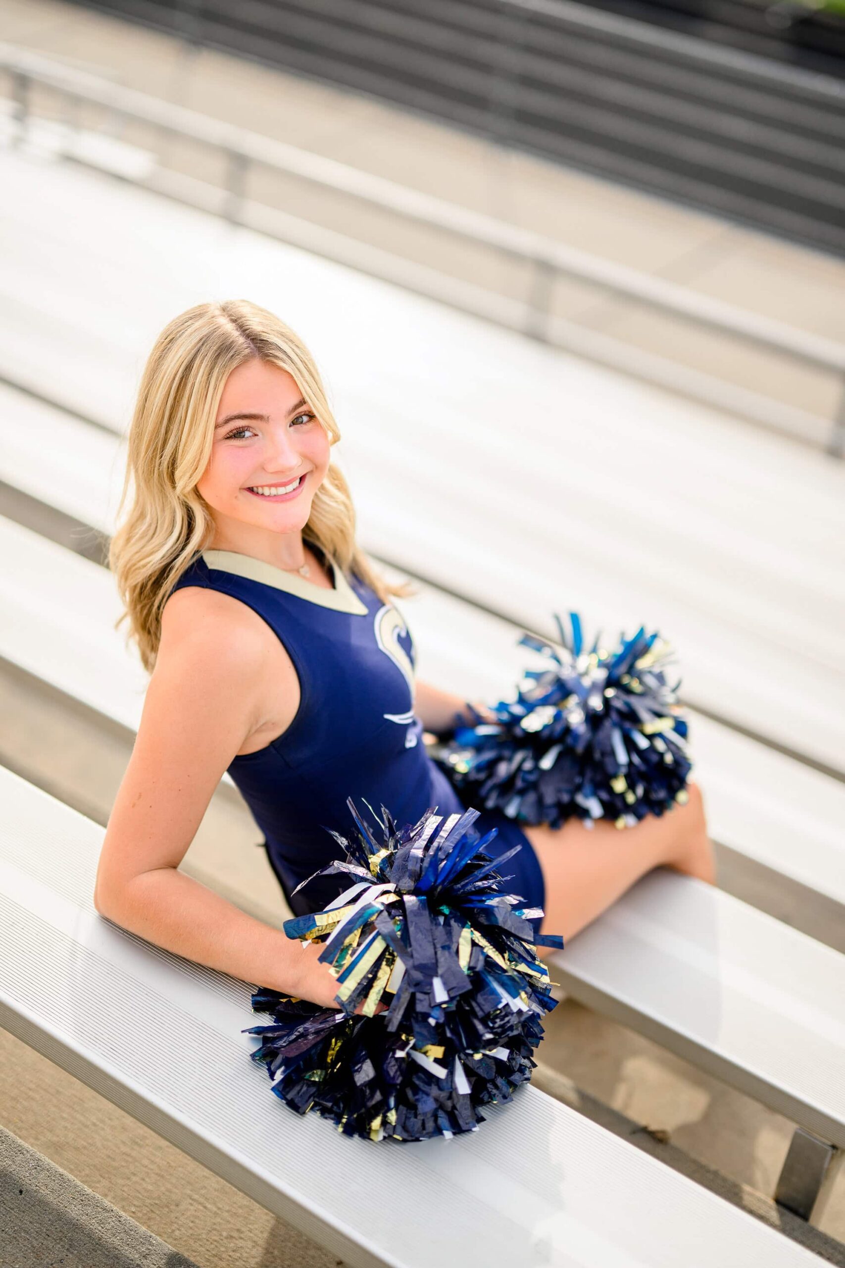 A cheerleader from Cuthbertson High School leans back against the bleachers, holding a pom in each hand while looking relaxed and cheerful.