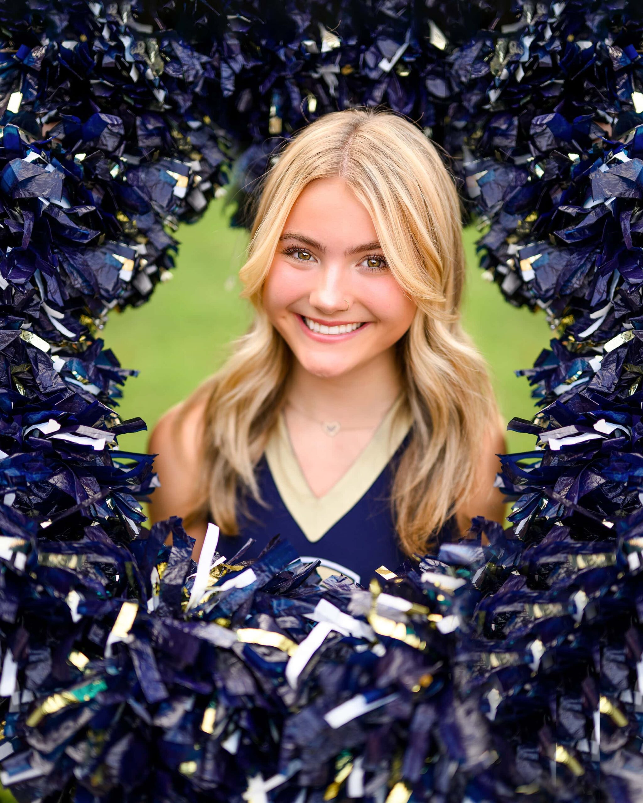 A blonde senior cheerleader from Cuthbertson High School poses in the center of a pom-pom ring, with poms forming a circle around her head. Senior Cheer Photos.
