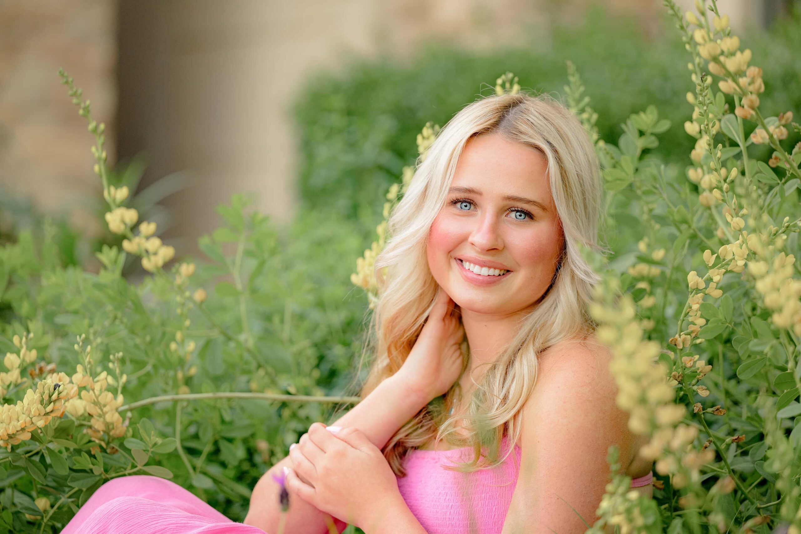 Surrounded by colorful blooms, Kait sits softly with one hand gently resting by her neck, capturing a timeless and elegant senior photo moment.