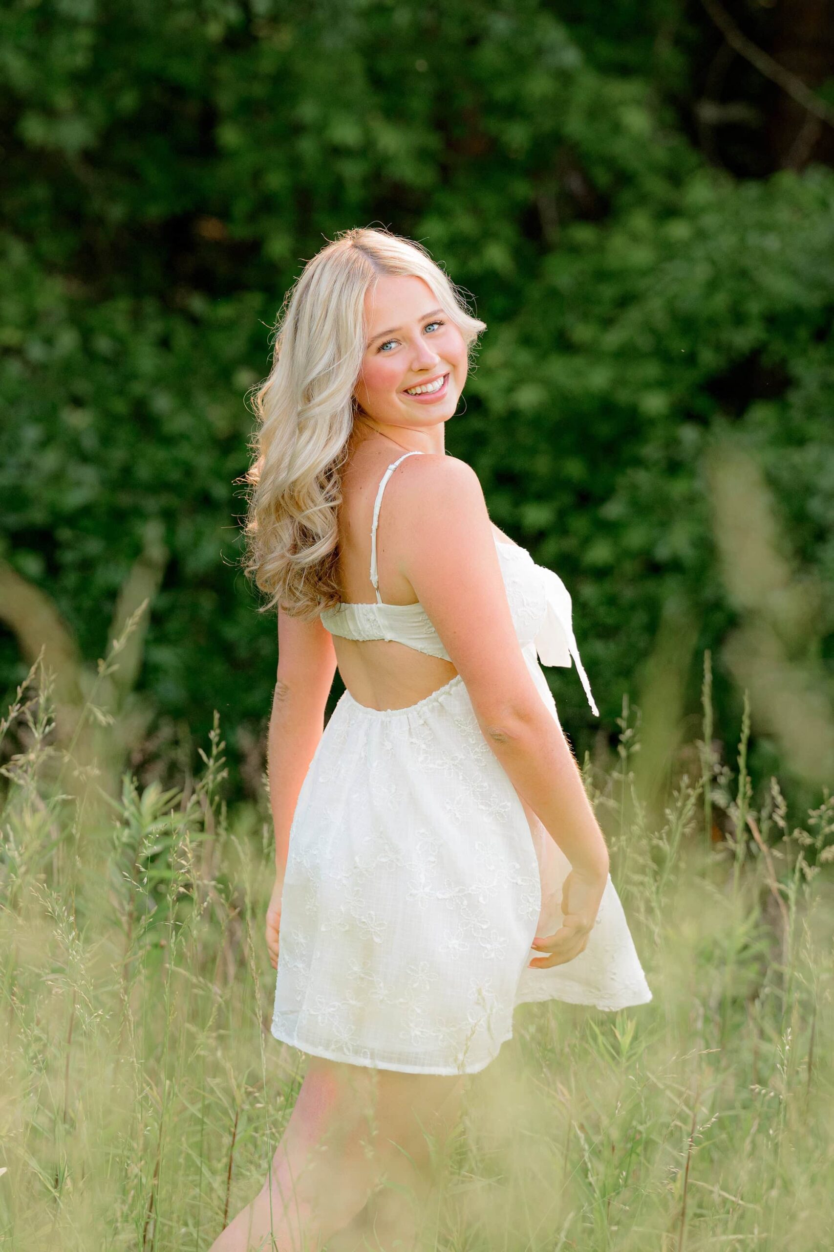 Captured in a side-profile full-body pose, Kait lifts her graduation cap high above her head in excitement as the sun glows brightly above her.