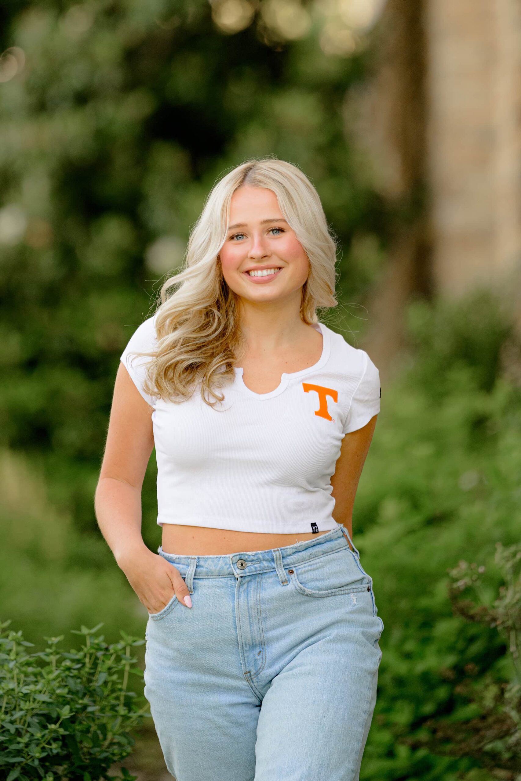 A close-up shot of Kait walking with a bright smile, radiating fun and excitement. Her blonde hair flows as she moves, capturing the joy of a Charlotte senior celebrating her final year.
