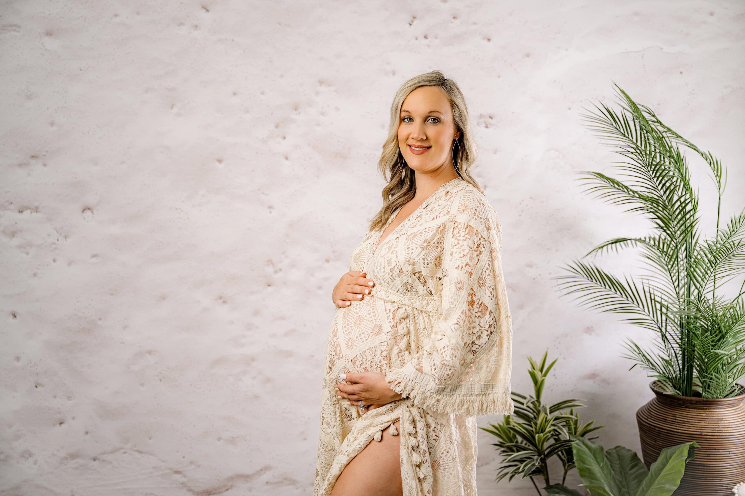 A side-profile maternity portrait in a Waxhaw studio, capturing the mom’s peaceful expression as she cradles her belly and looks directly into the camera. The boho-inspired setup with warm neutrals and greenery enhances the serene feel.