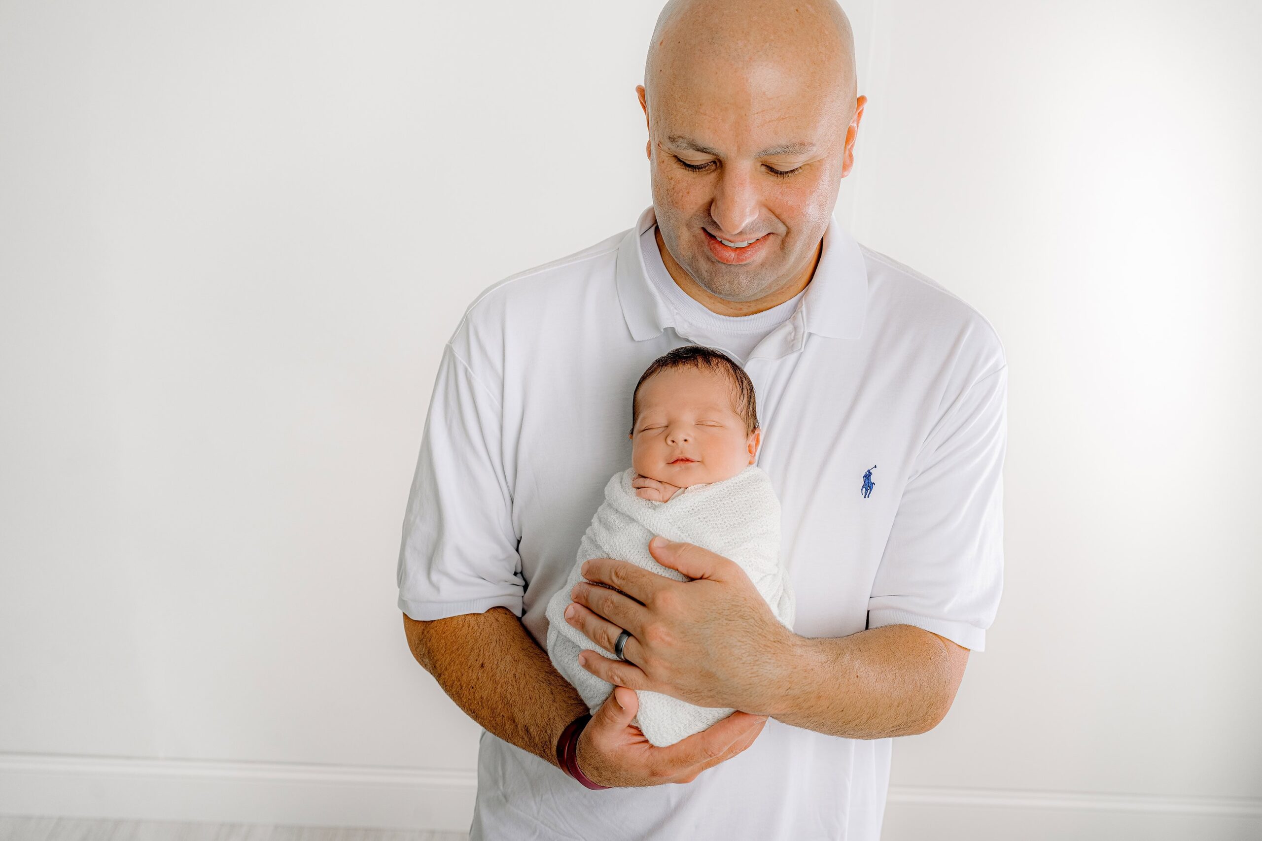 Dad holding newborn son in his arms, smiling down lovingly at him, in my Waxhaw studio. The warmth of family connection shines through.
