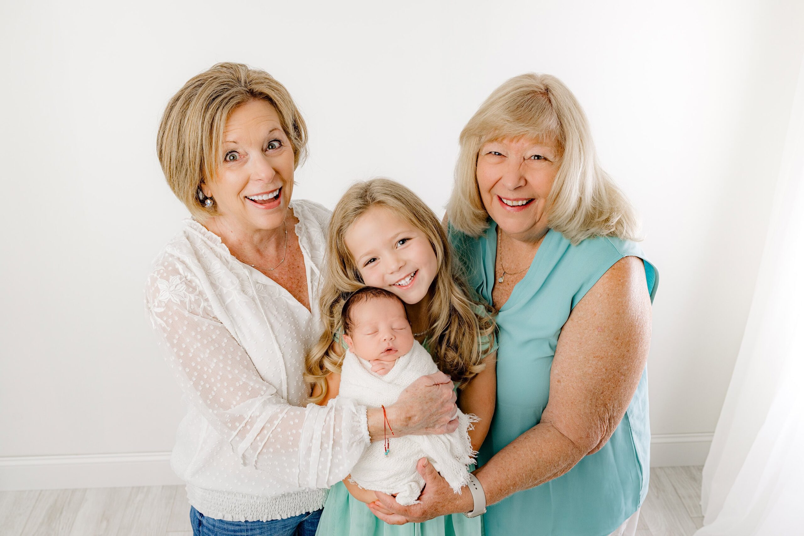 With her head gently tilted toward her newborn baby brother, the little girl cherishes the moment while both grandmothers laugh with pure joy. Their shared grandparent love shines in this heartwarming family portrait taken in my Waxhaw, NC studio.