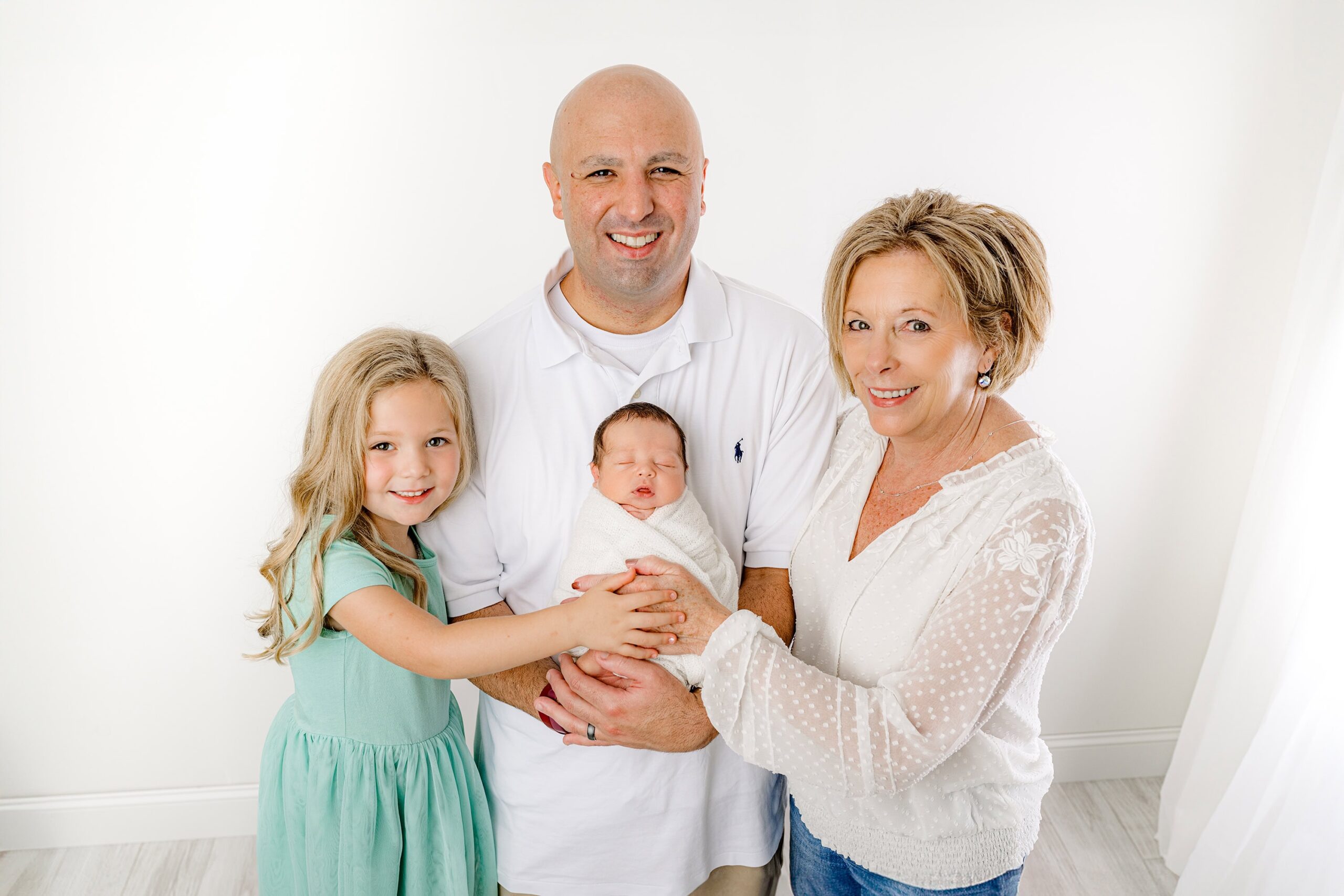 In this touching portrait, the dad holds his newborn baby with his mother on his left and his daughter on his right, surrounded by love and connection in my Waxhaw, NC studio.