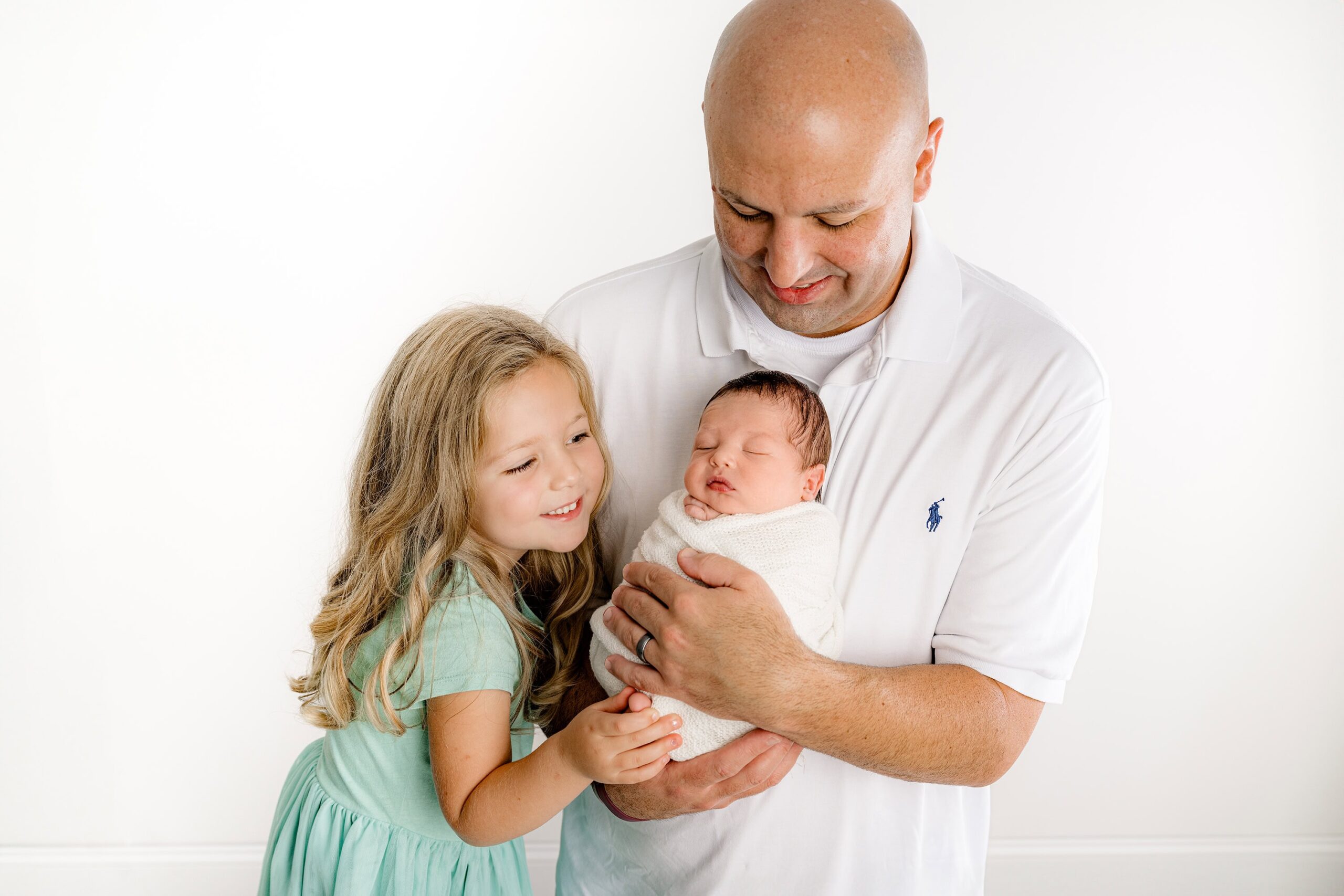 Dad holds his newborn son while he and his daughter lovingly gaze down at him, captured in my Waxhaw studio. A moment filled with joy and tenderness.