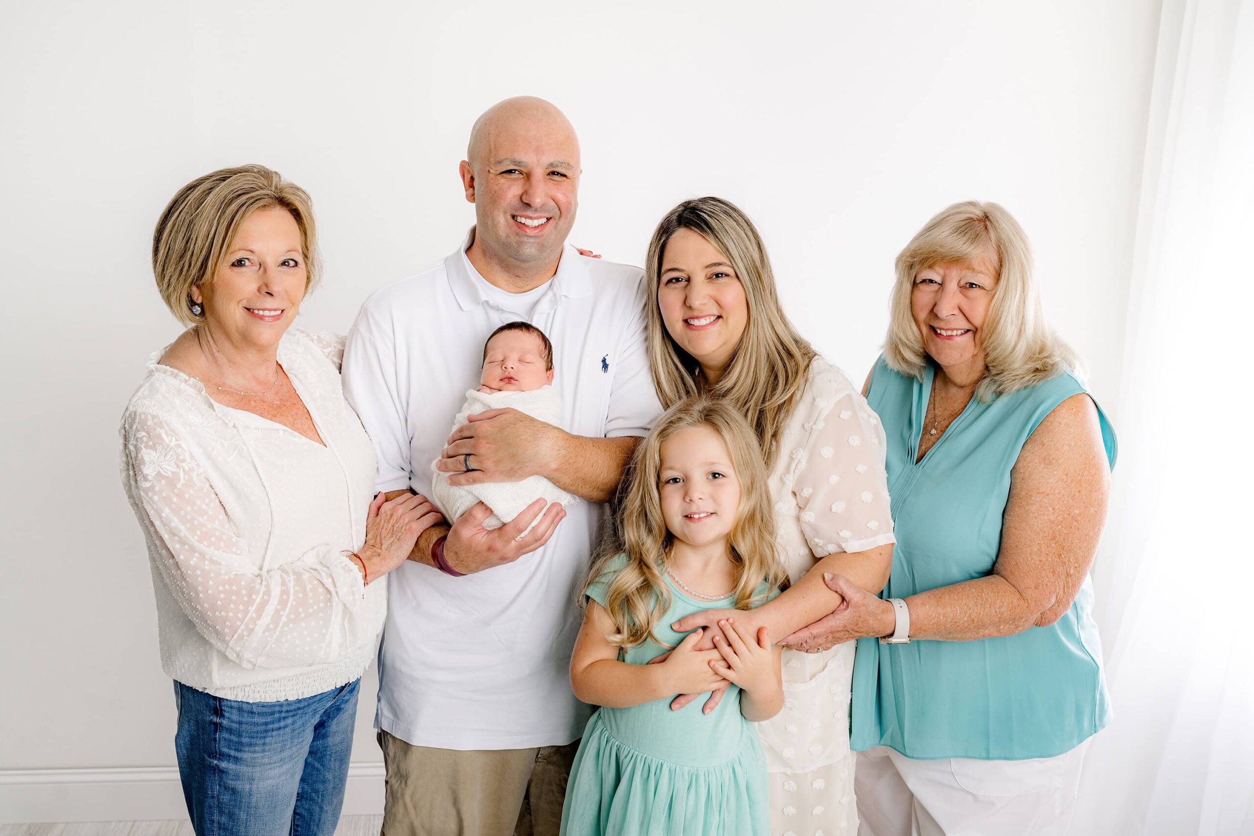 The full family gathers together in this heartfelt portrait, with the dad holding the newborn while both grandmothers stand proudly on each side. This moment captures the pure essence of grandparent love in the heart of the family.