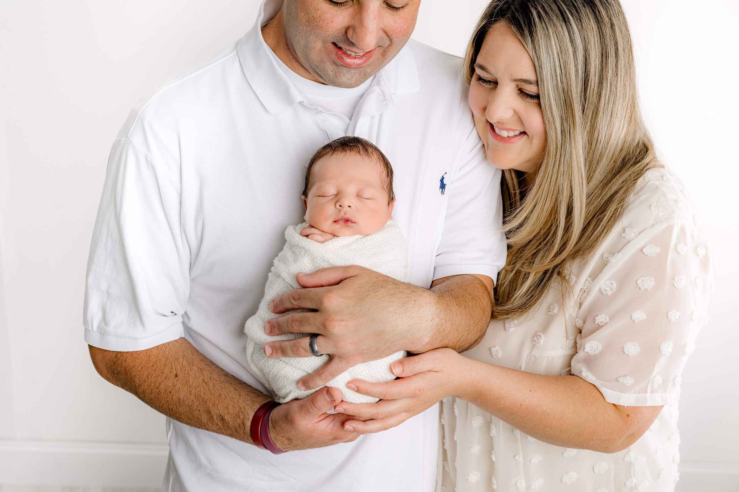 Dad gently cradles his newborn baby boy, while both mom and dad look at their son with pure love and adoration in my Waxhaw studio.