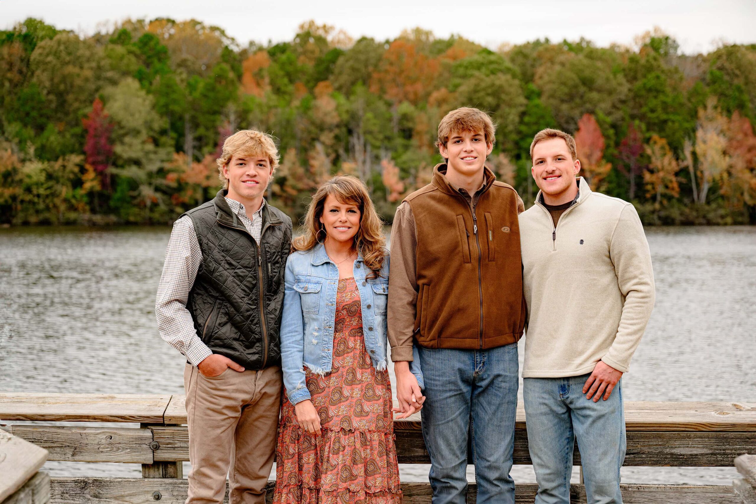 mom of three boys stands by a lake for a family photo