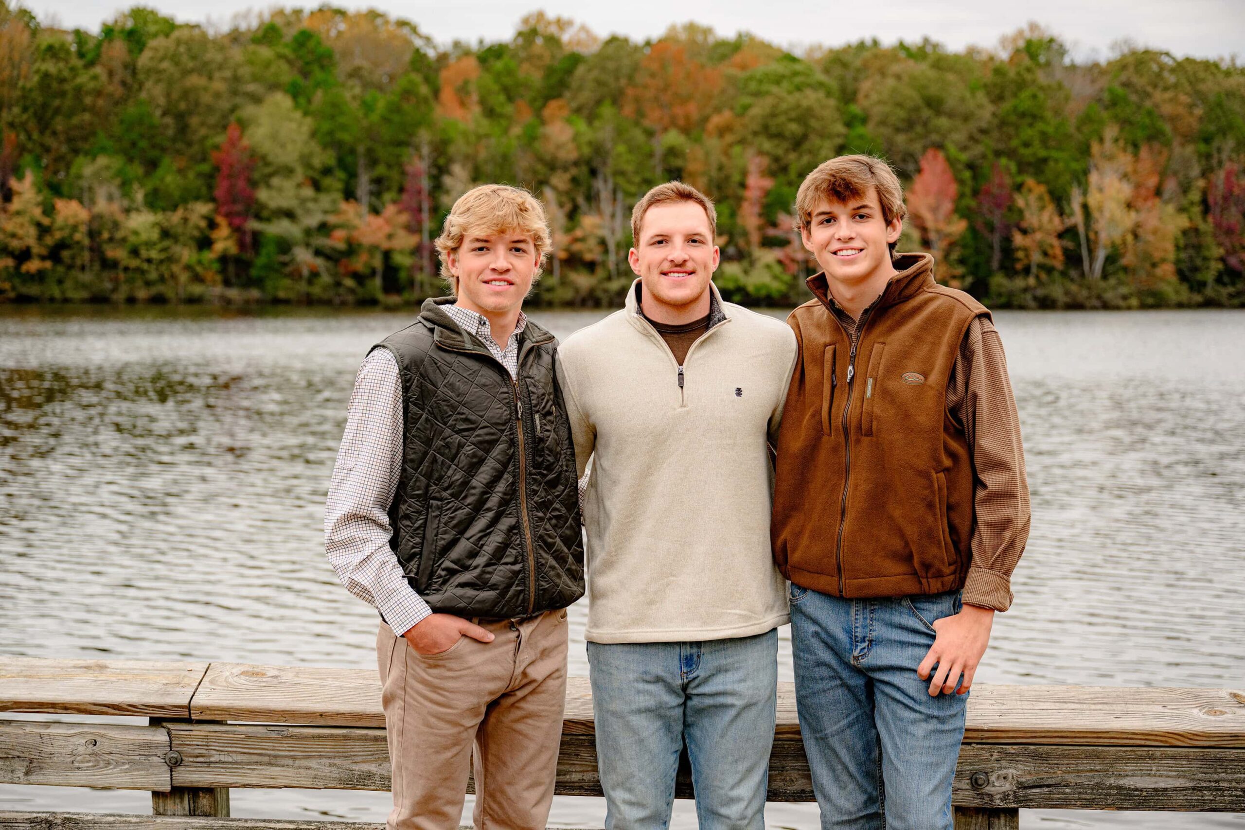 3 brothers all dressed in natural colors stand together with the lake behind them