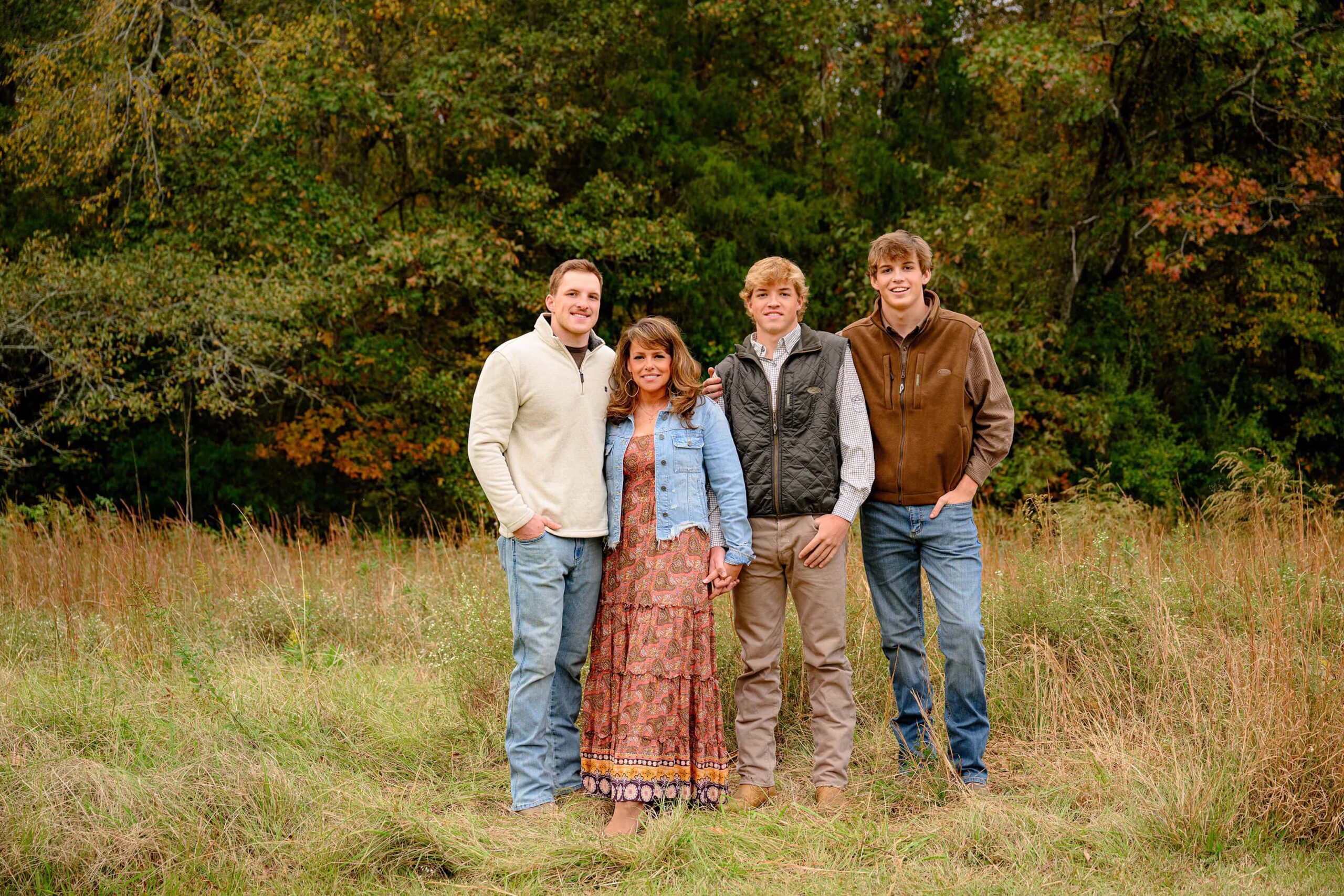 mother of three sons stands together in a tall grass field with fall leaves behind them