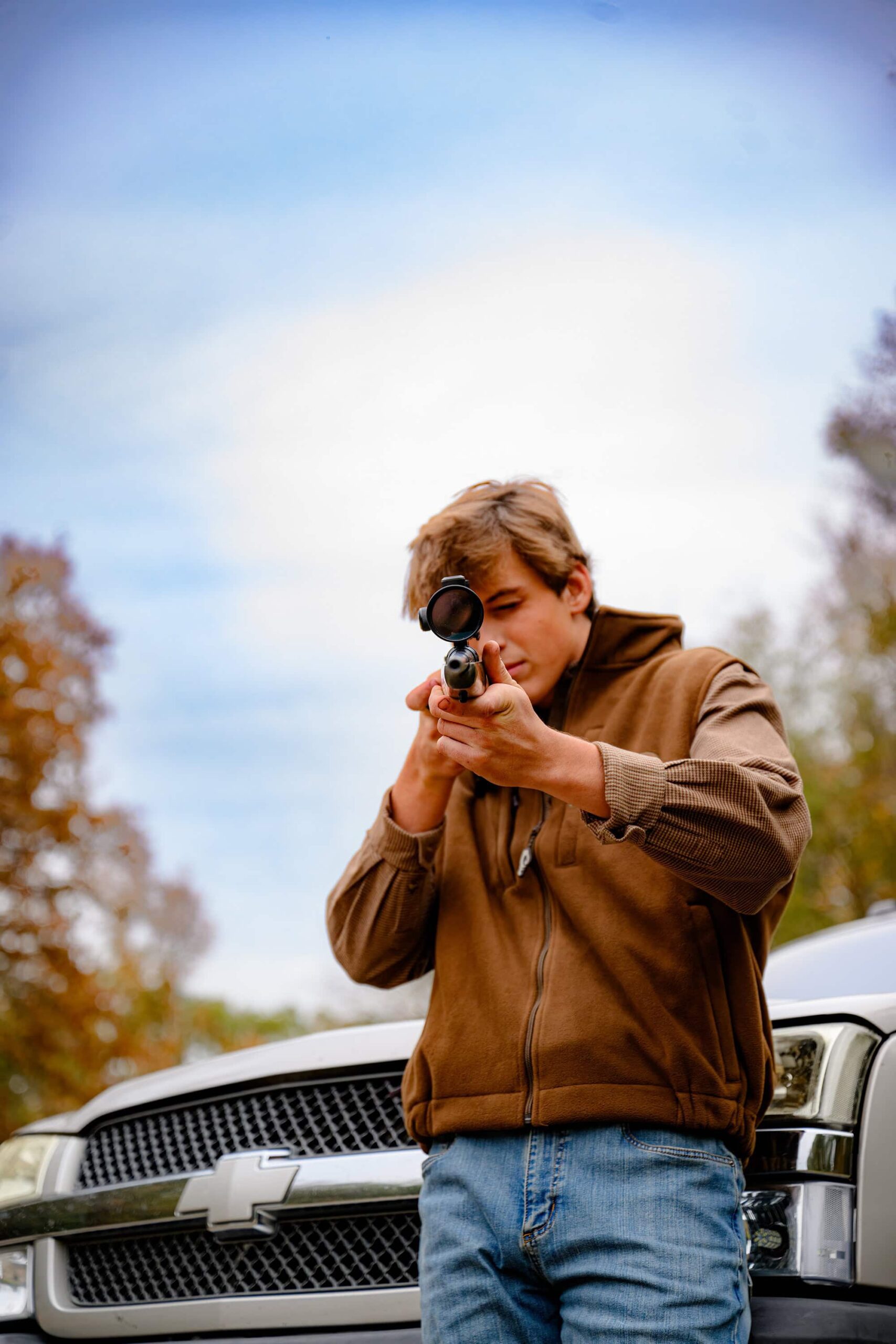 like a true country boy this parkwood poses with his rifle wearing jeans and a brown shirt and vest