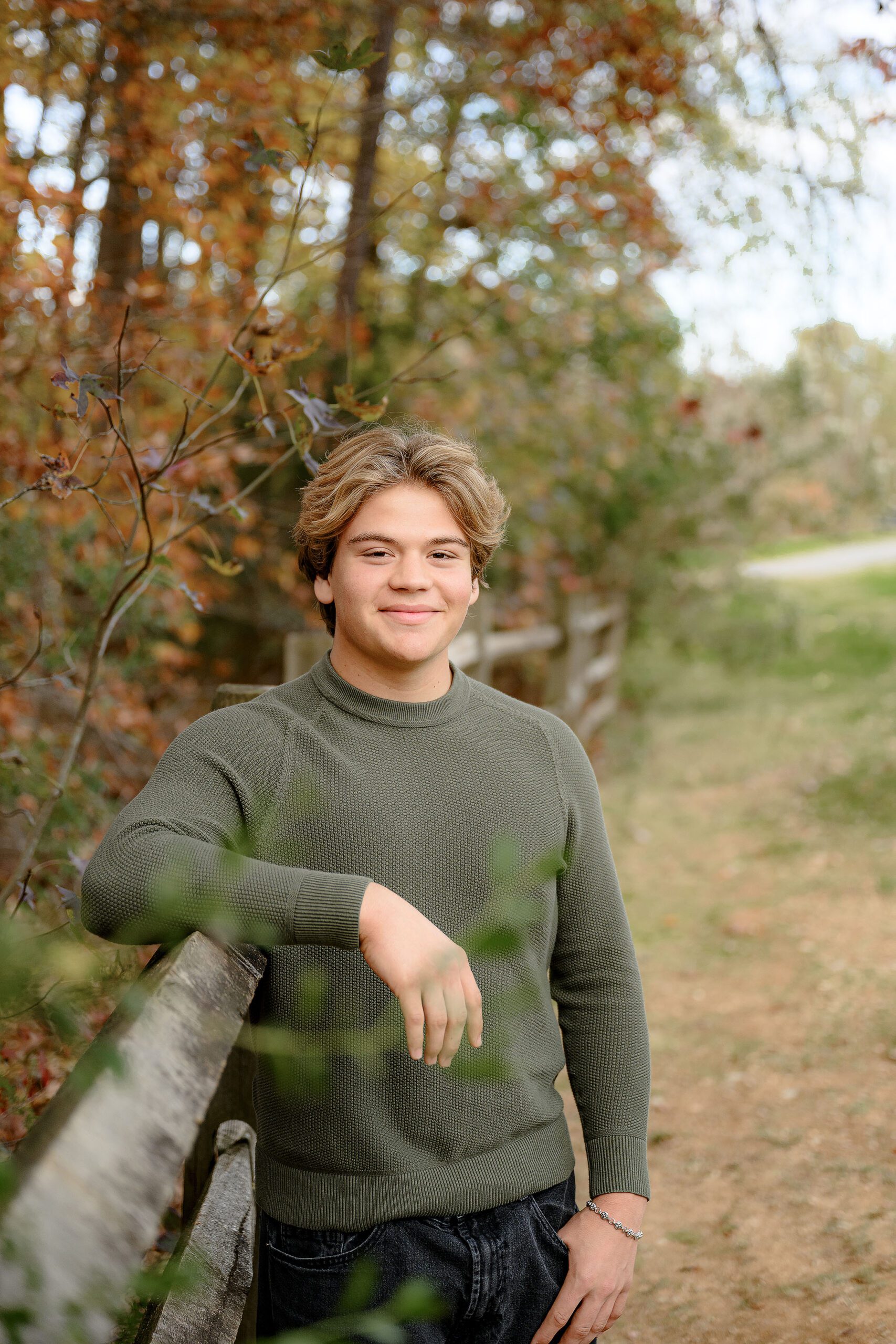 cuthbertson senior leans agains a fence wearing a green shirt in a waxhaw park