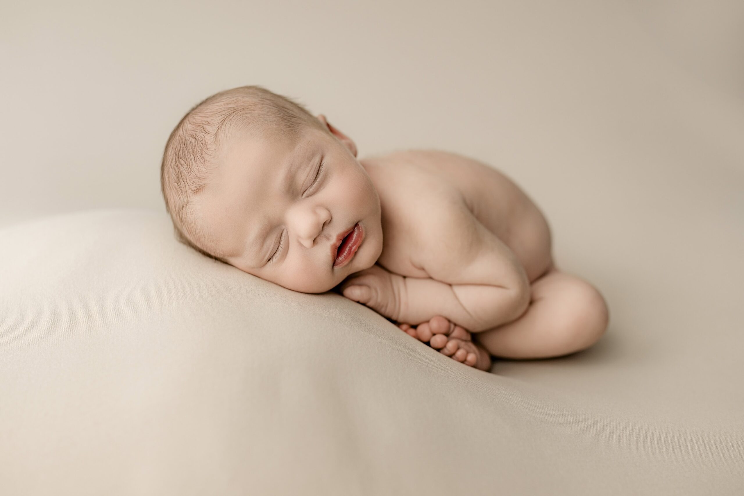 posed newborn laying on cream background