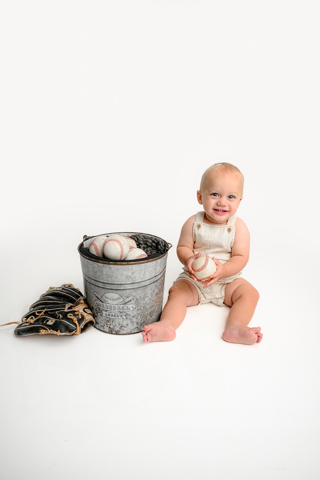 one year old boy sits holding a baseball as a nod to his newborn photoshoot