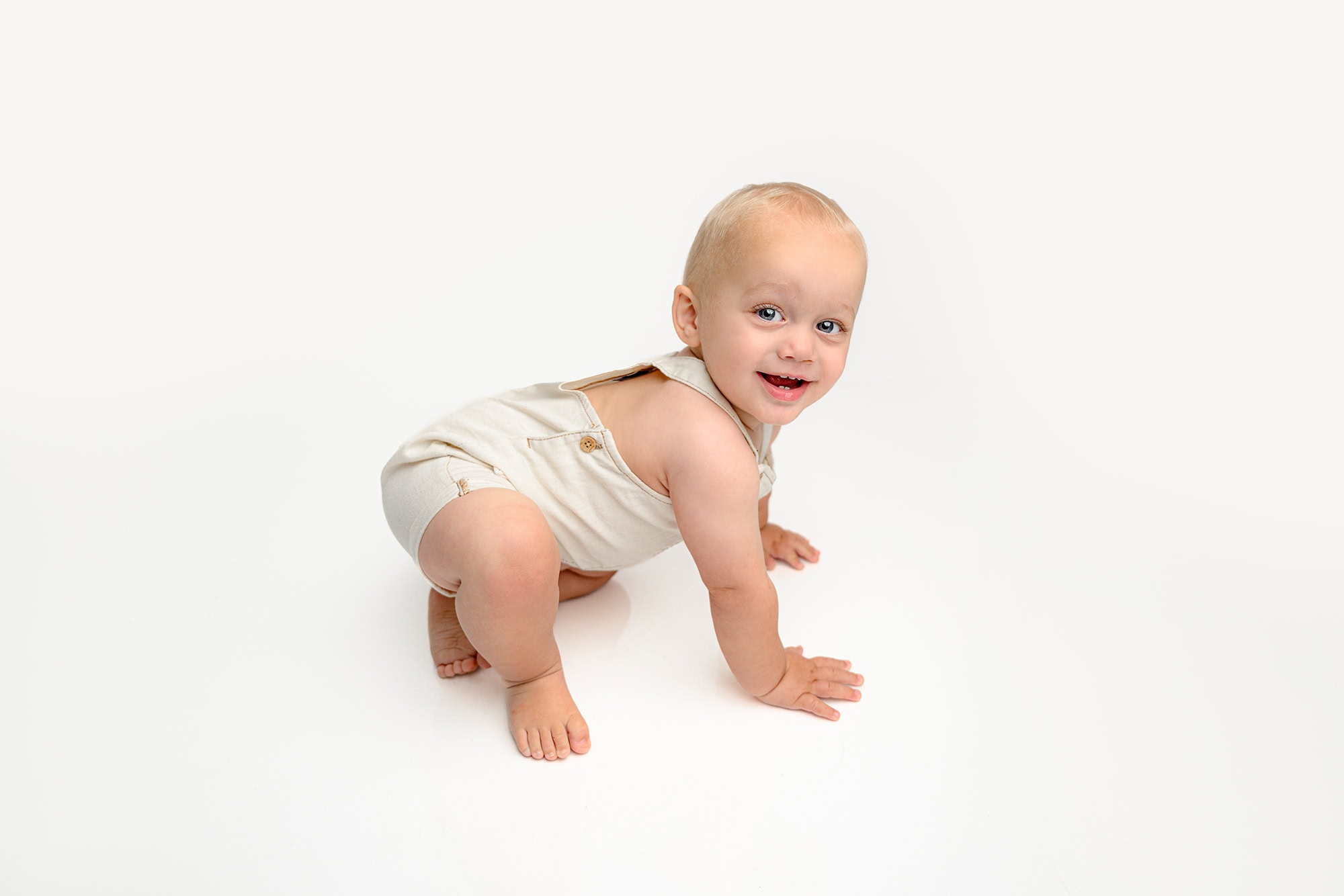 Little one year old boy in cream overalls at first birthday photoshoot