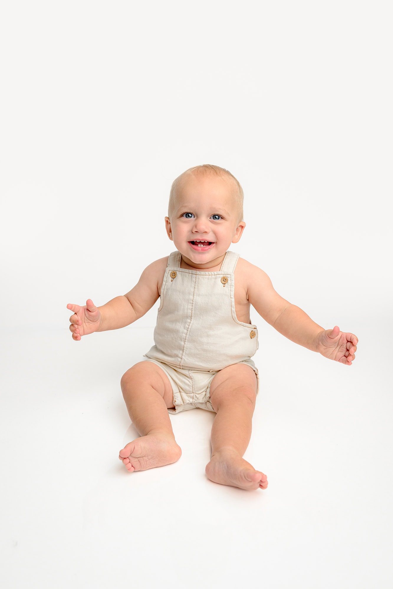 milestone photo of little boy in cream overalls on a white studio set up