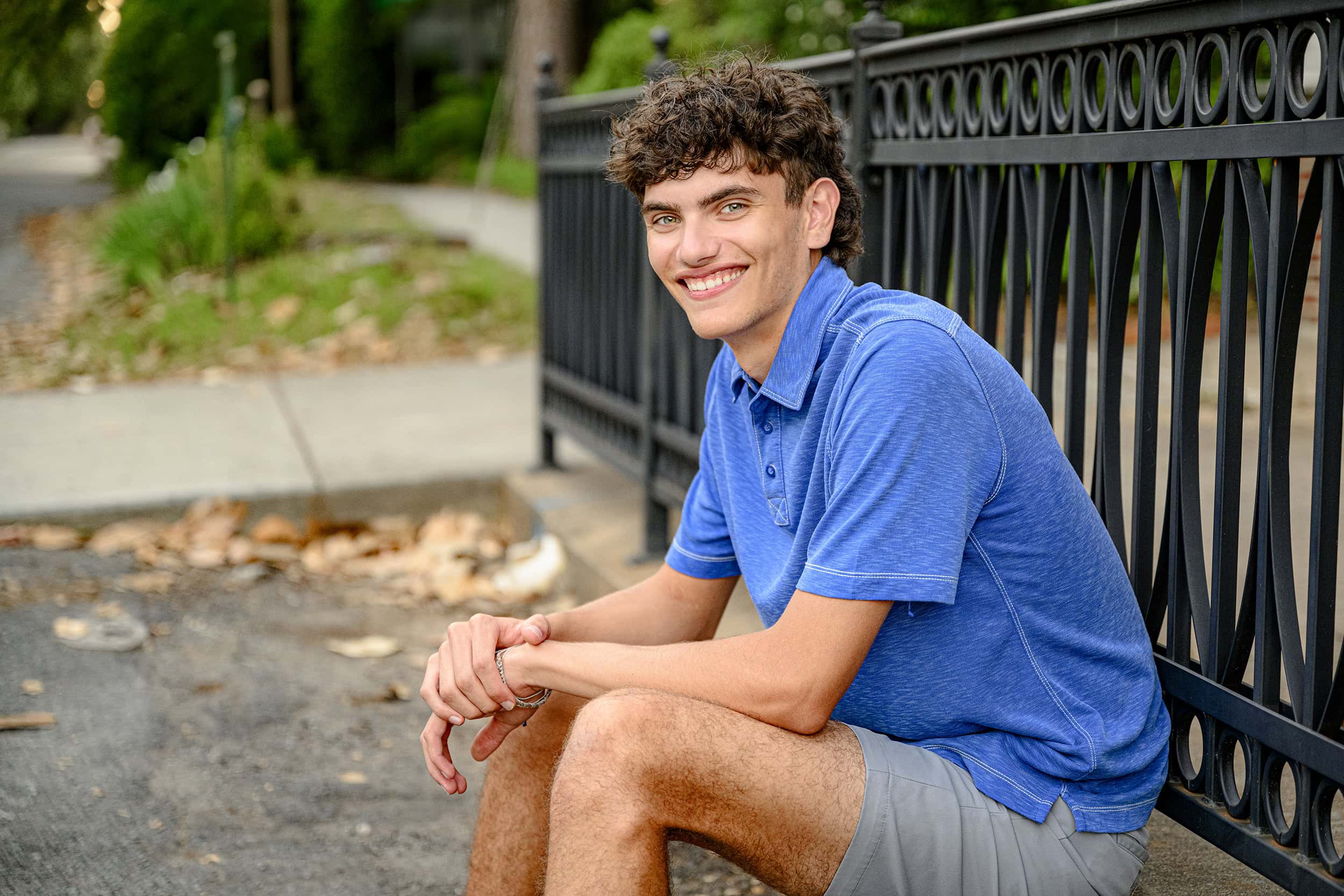 senior boy from waxhaw smiles as he sits on ledge in downtown location