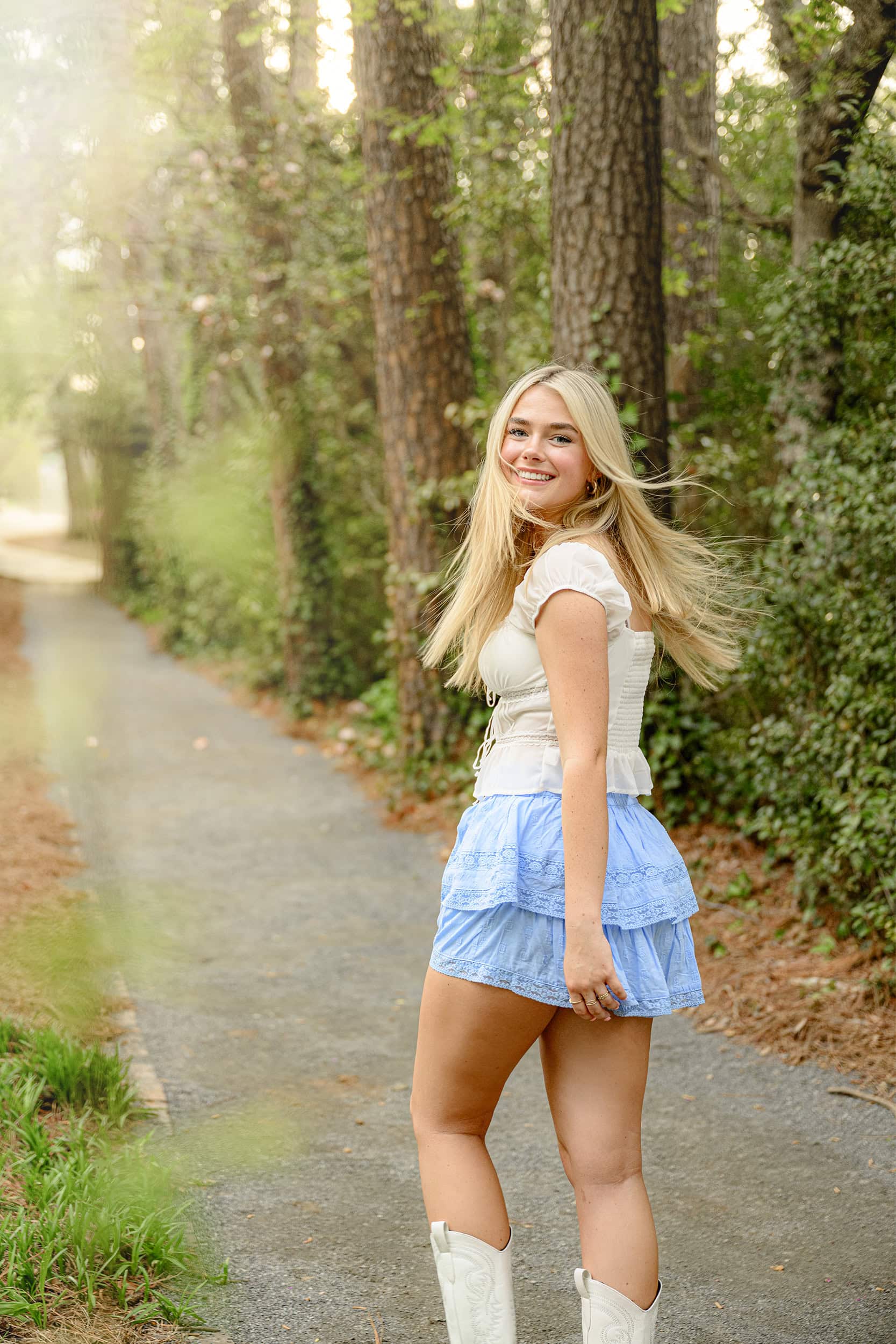 casual relaxed smile as this charlotte graduate looks back over her shoulder during senior photos while wearing a white top and blue skirt