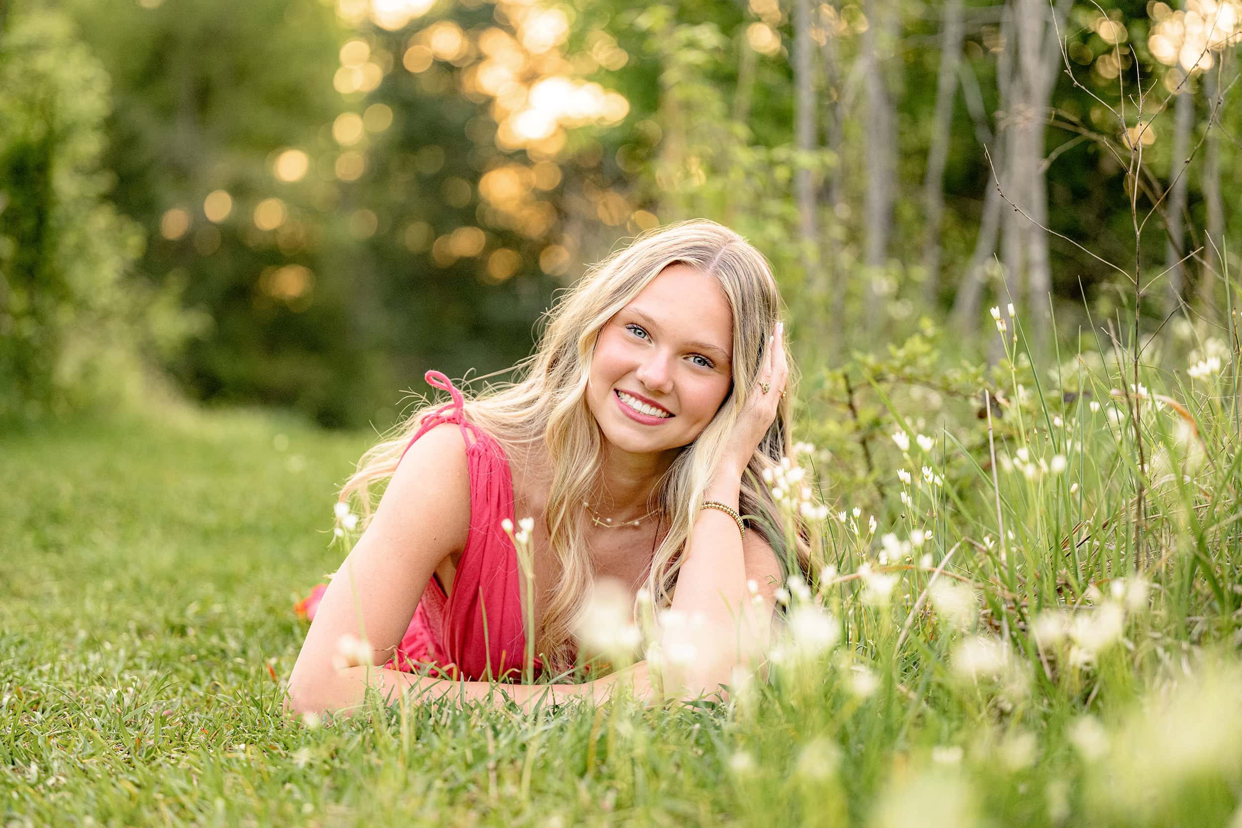senior girl wears bright pink dress while laying in a charlotte field