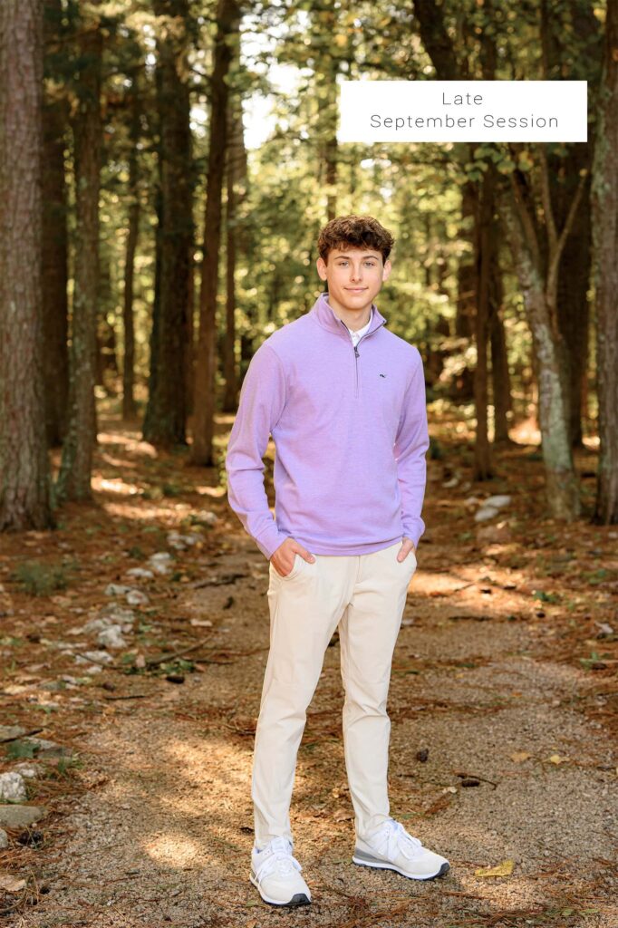 graduate dressed in purple stands on a pathway surrounded by fall colors of late september