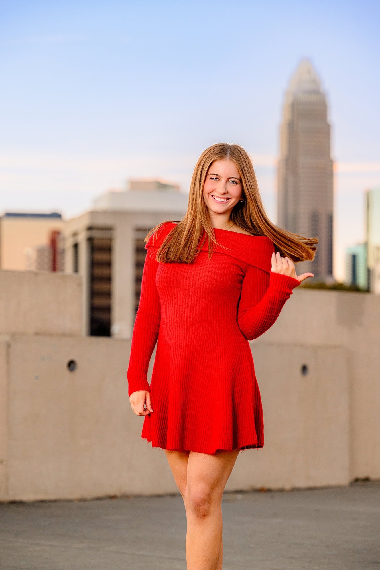 Charlotte Grad on Rooftop location wearing a seasonal red sweater dress twirling her hair