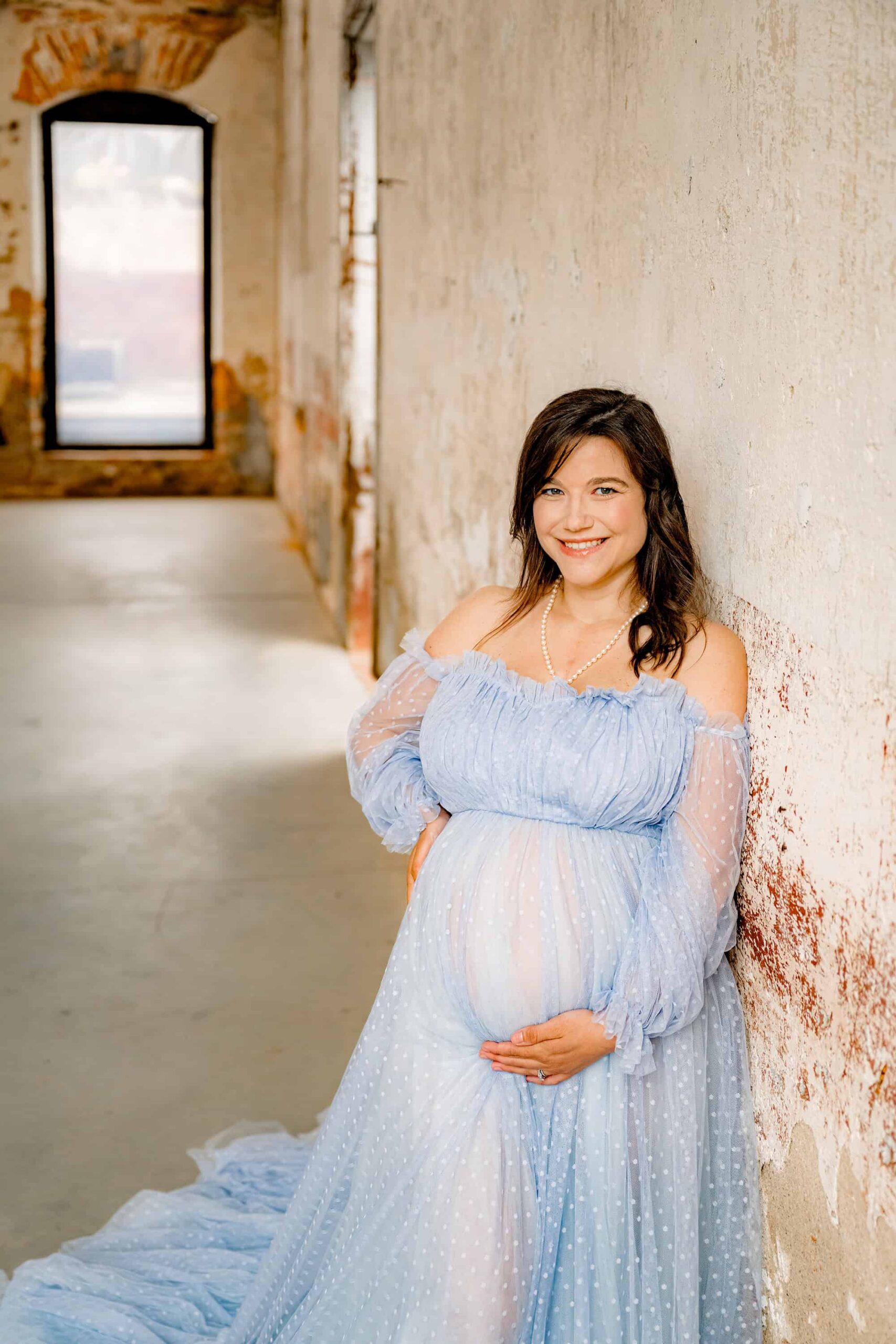 expectant mother is dressed in a blue dress leaning against a wall