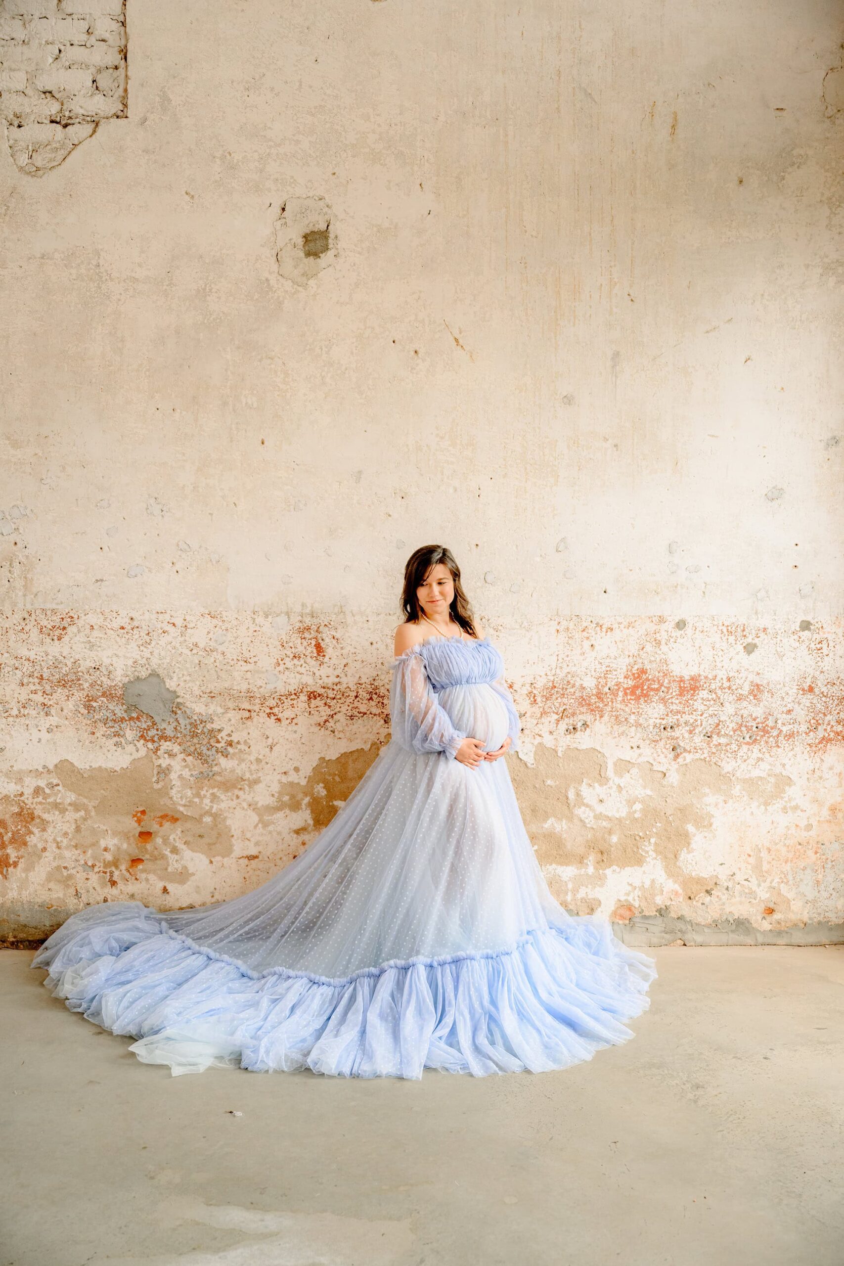 charlotte pregnant mother holds belly wearing a full skirt maternity dress with a historic wall behind her
