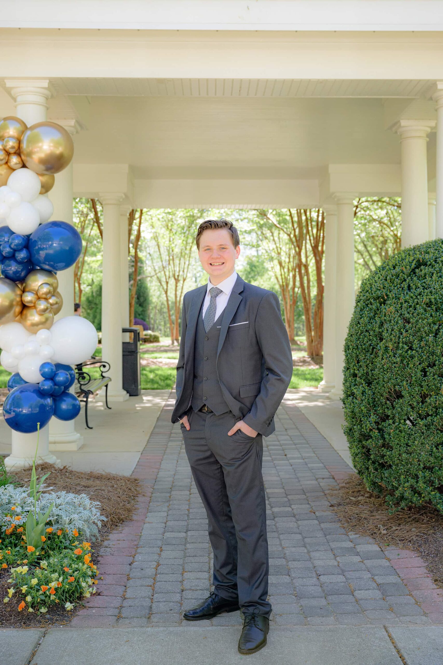 guy dressed in full 3 piece suit and black shoes for senior prom photos under a pavilion