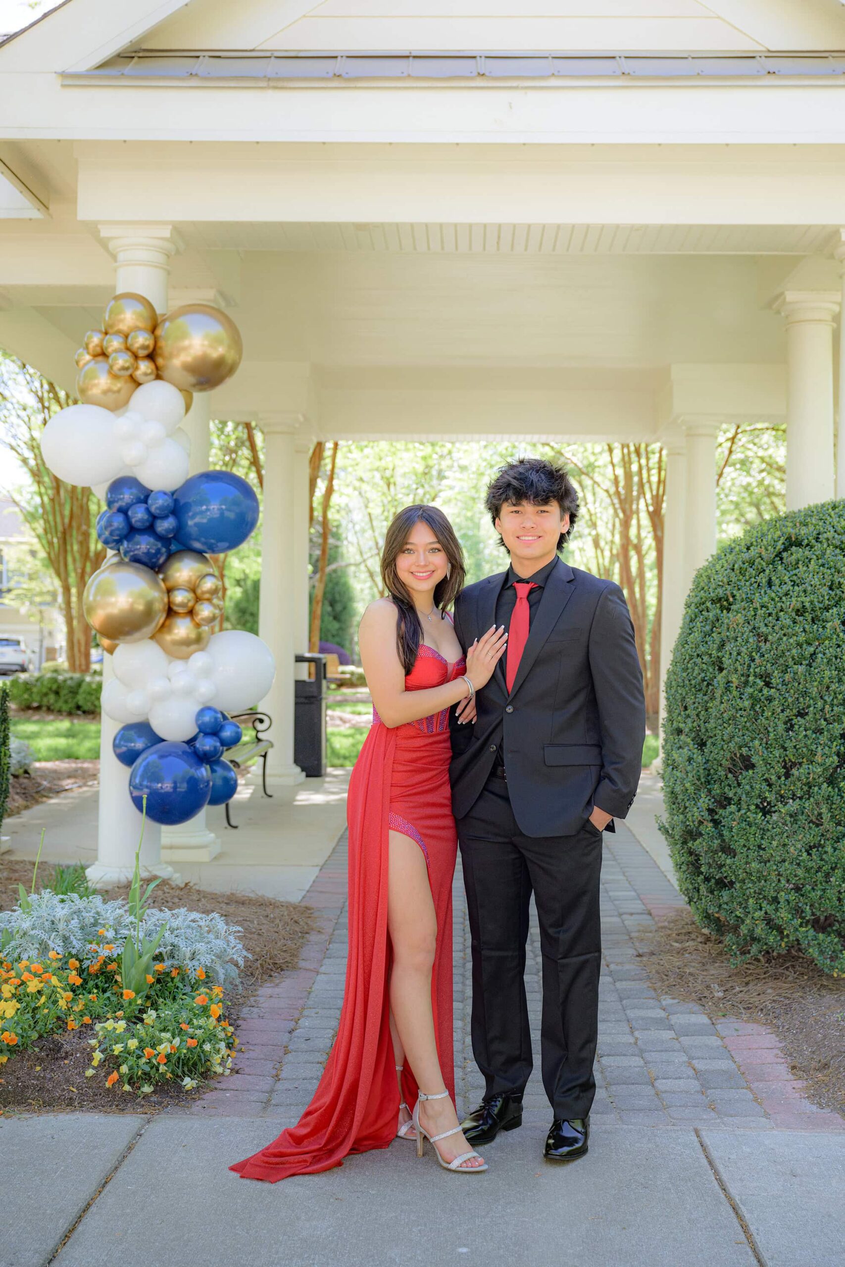 boy wears a black suit with a tie that matches his prom date wearing a red dress