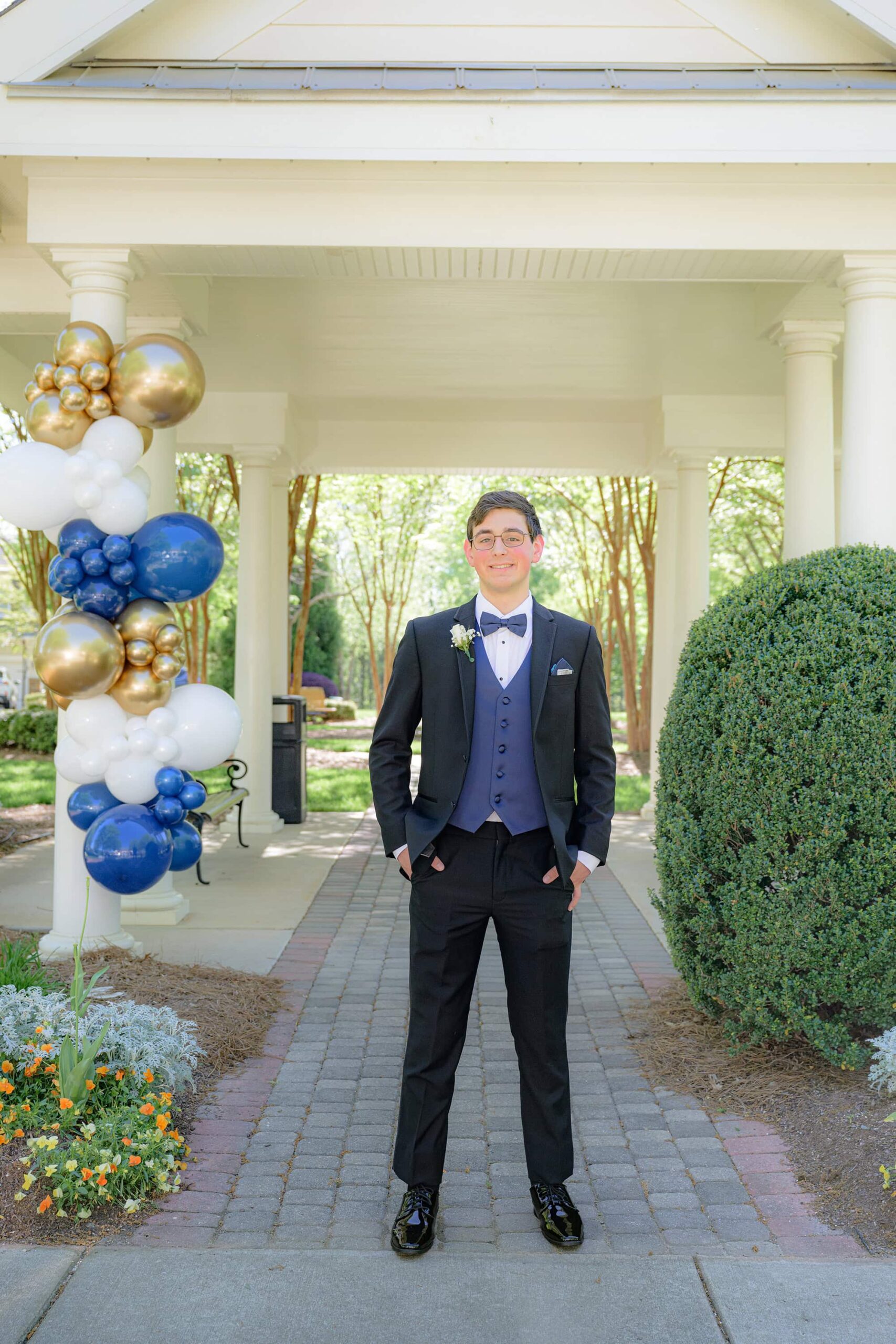 senior prom photo of boy in a dark suite with navy accents under a pavilion