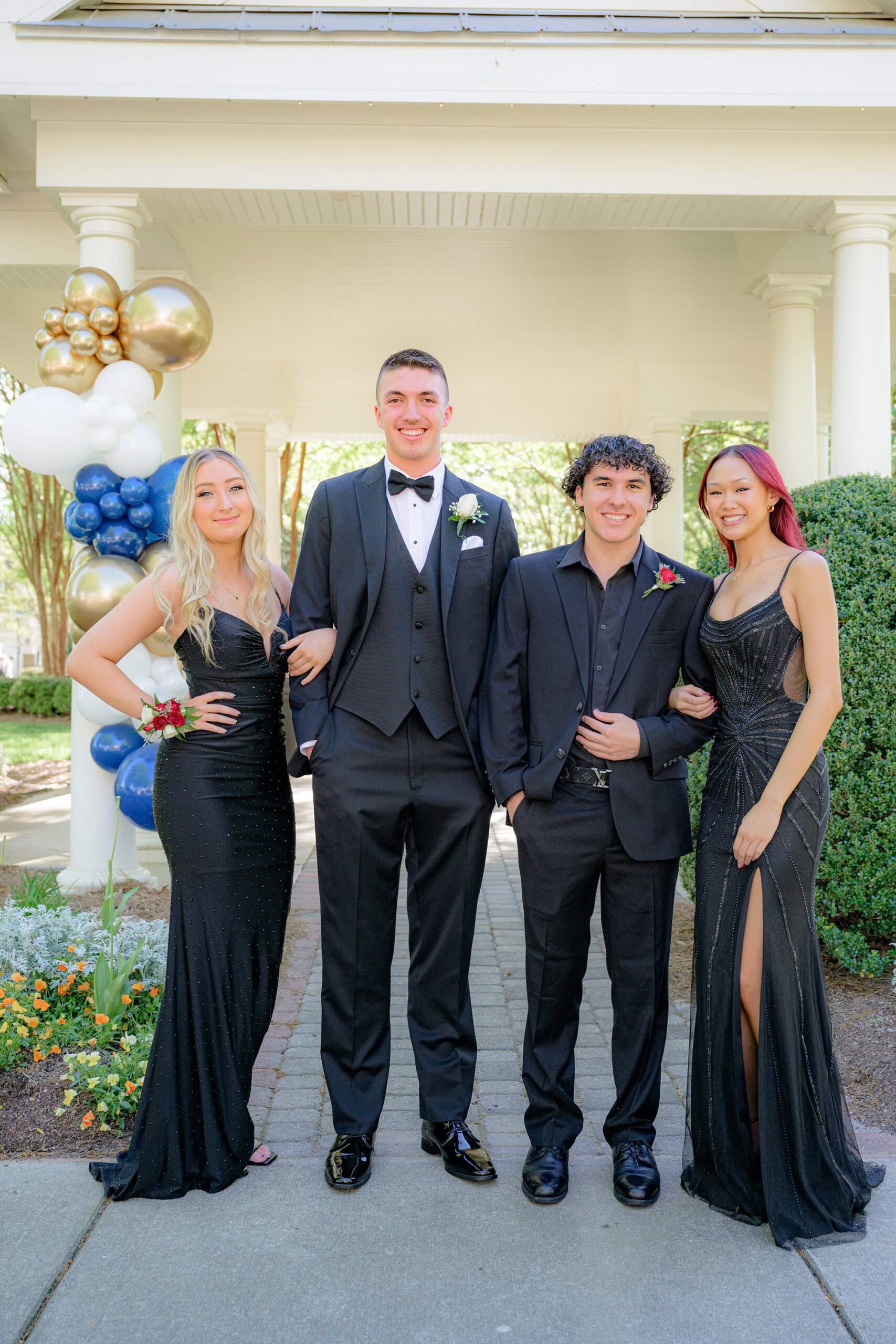 four graduates all dressed up for prom. girls are wearing black and boys are wearing black tux and suits