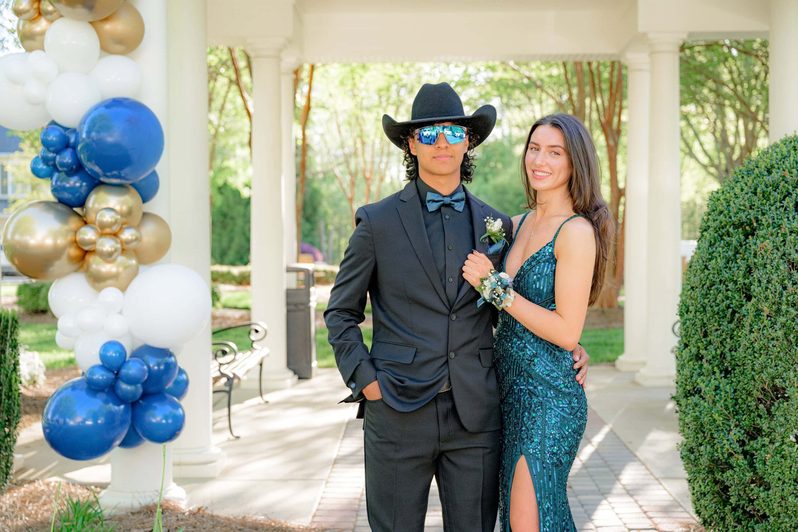 senior boy dressed in a black suite and green bow tie as well as sunglasses and a cowboy hat