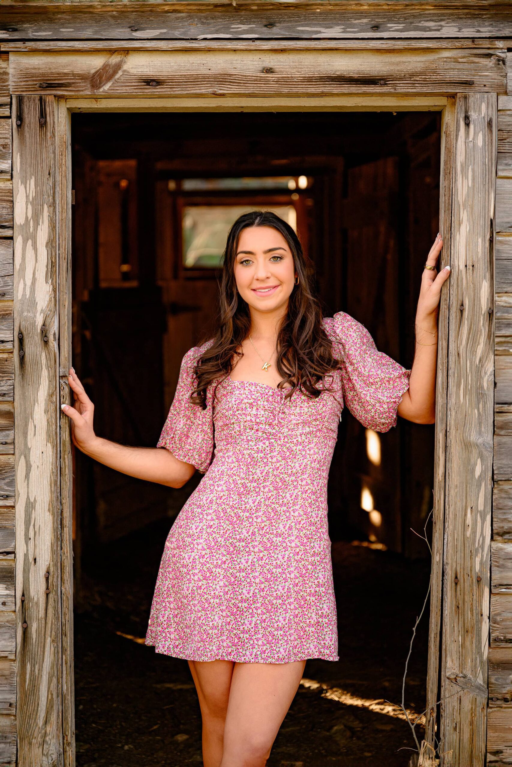 marvin high grad stands in doorway of a barn with her hands on the railing wearing a floral print baby doll dress