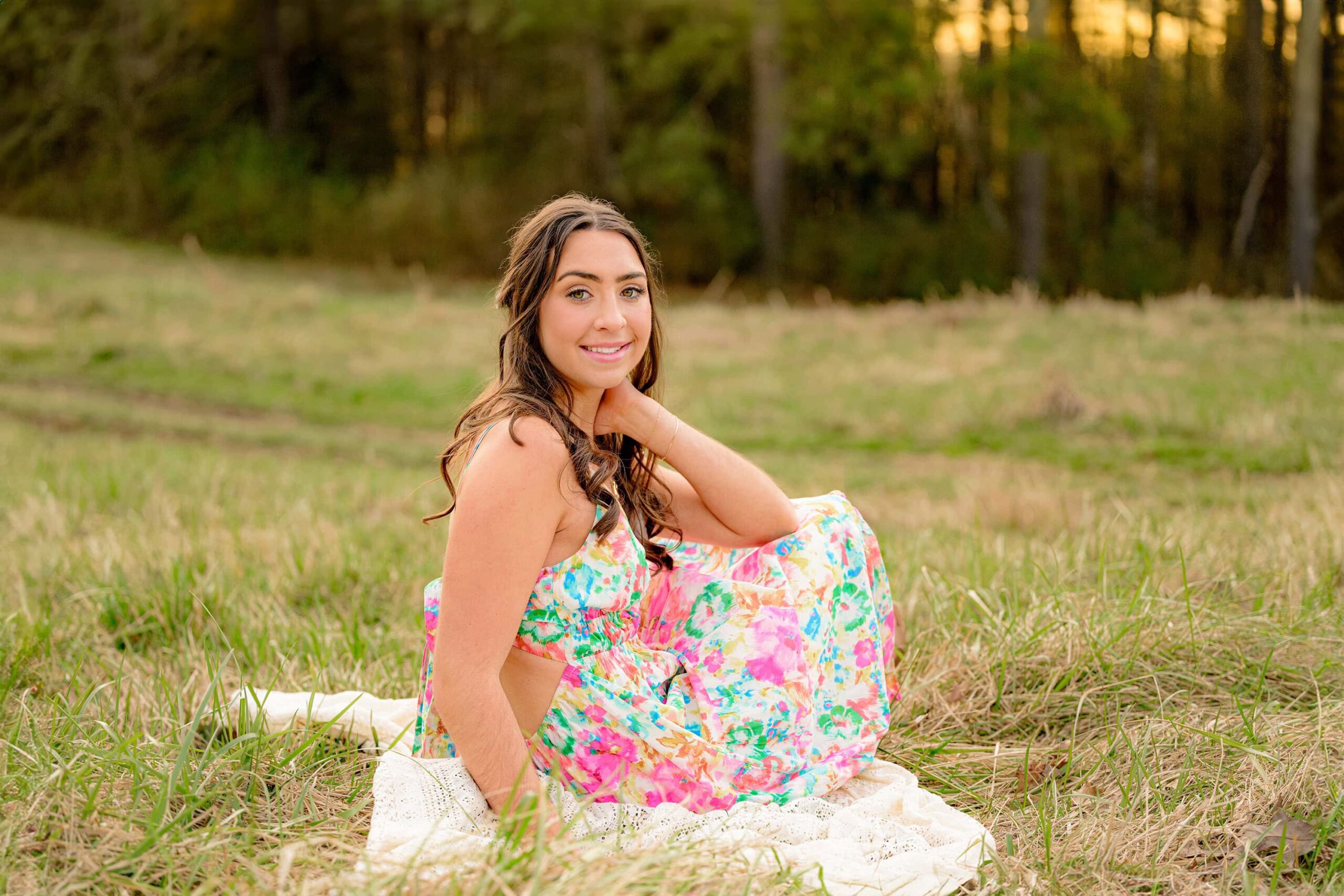 charlotte senior wearing a spring floral dress sitting in a field with her hair curled