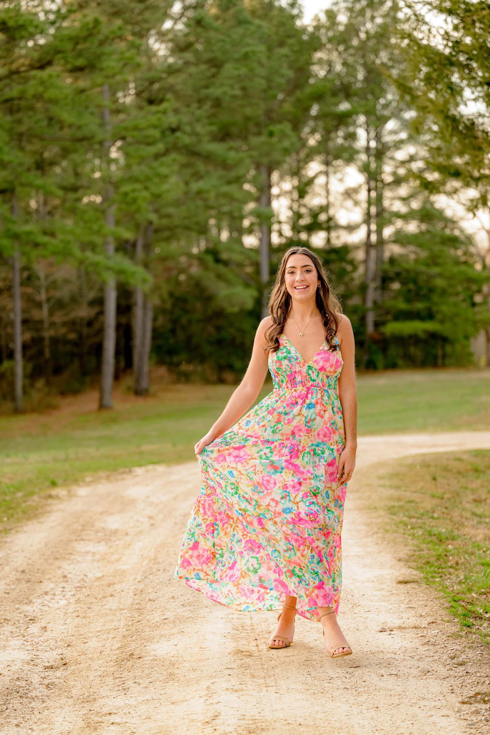 walking on a pathway at the ivy place farm this senior holds out her spring printed floral dress and smiles