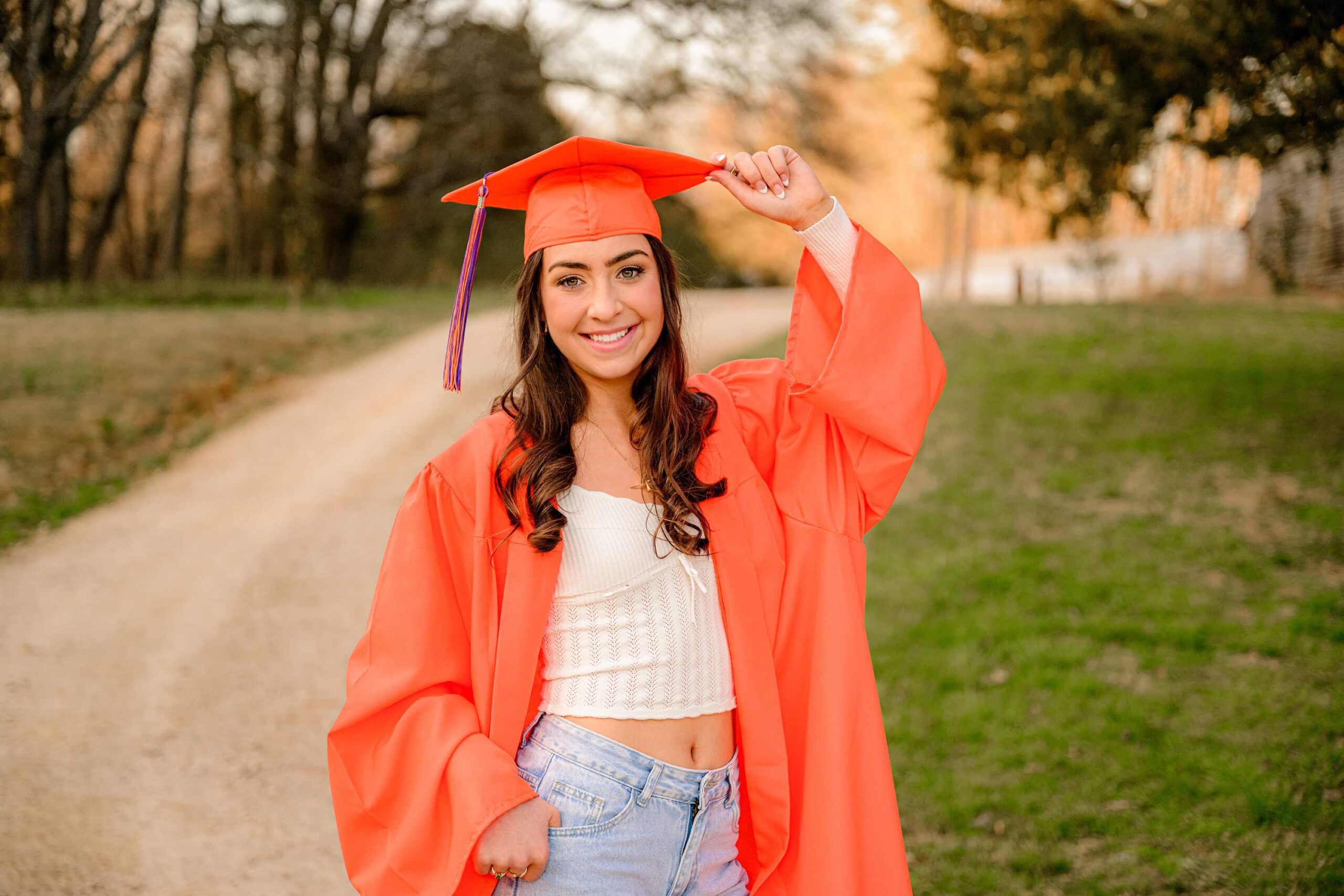 senior from marvin ridge high school wearing jeans and a white top with her orange cap and gown