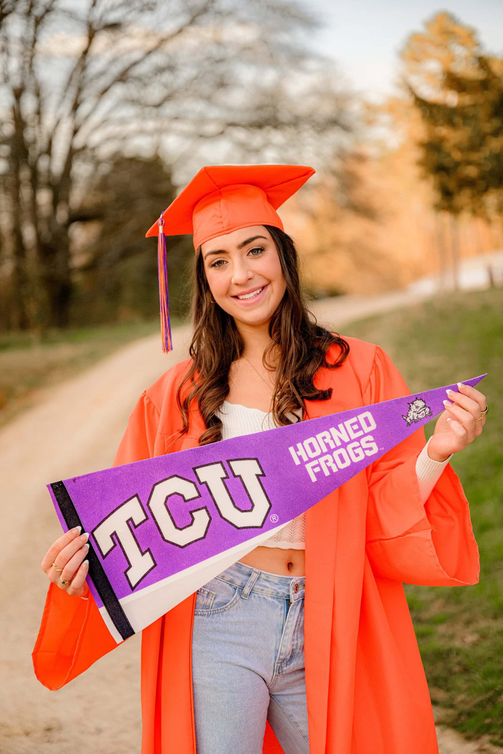 wearing her orange cap and gown senior poses with her future TCU pennant