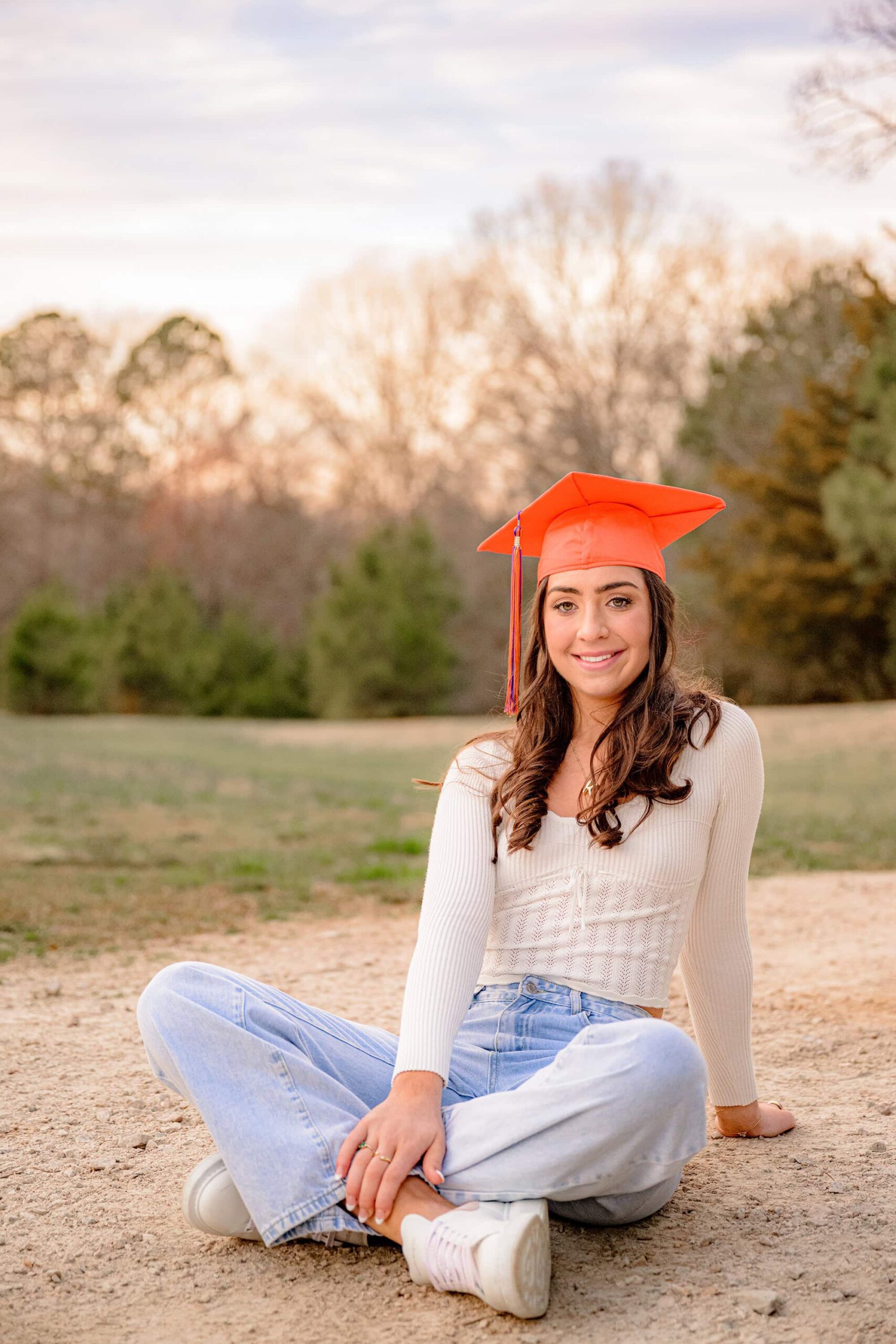 senior sits on a gravel pathway wearing her orange marvin ridge graduation cap
