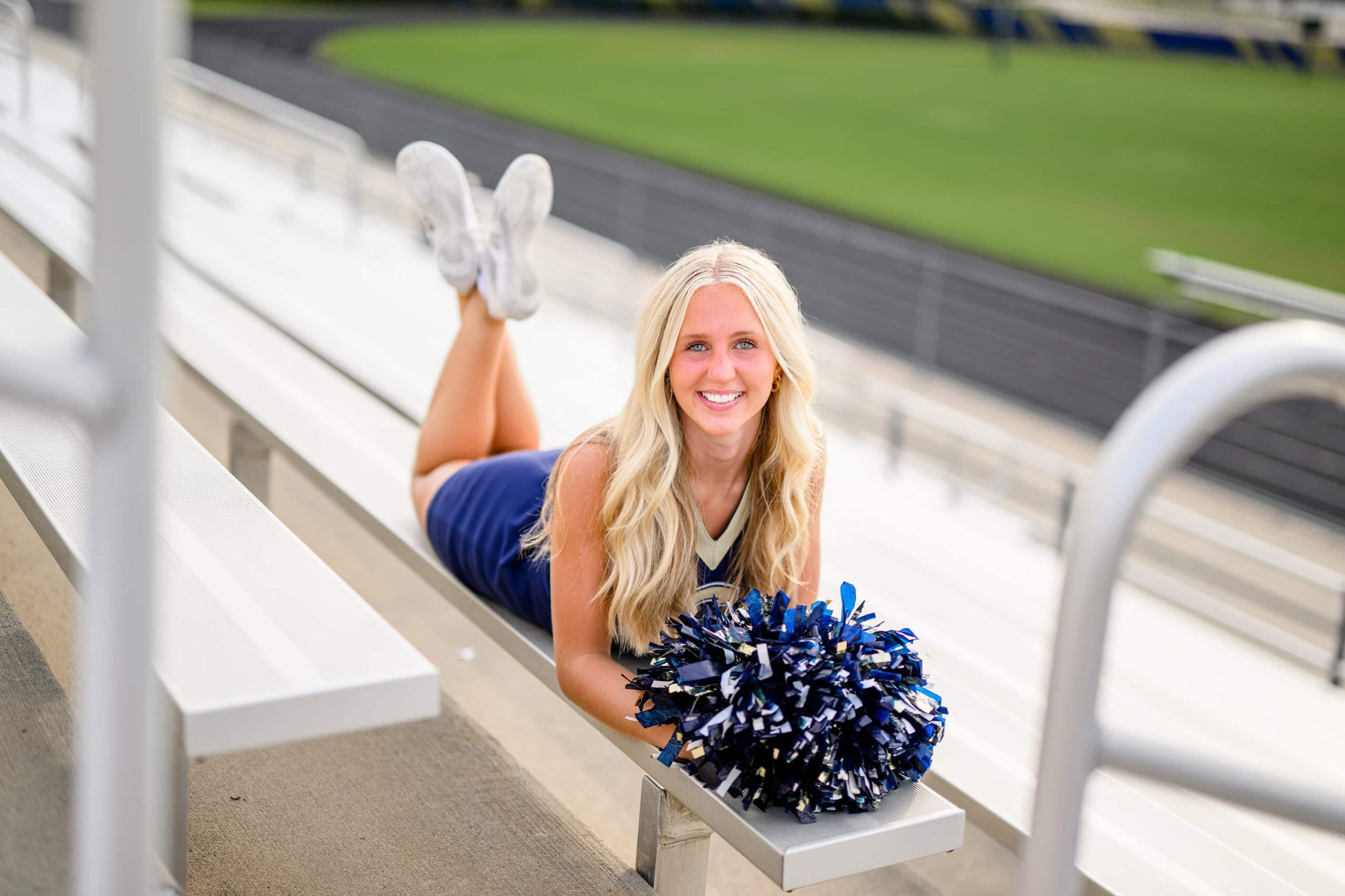 cuthbertson cheerleader lays on bleachers on her stomach with her poms in front of her
