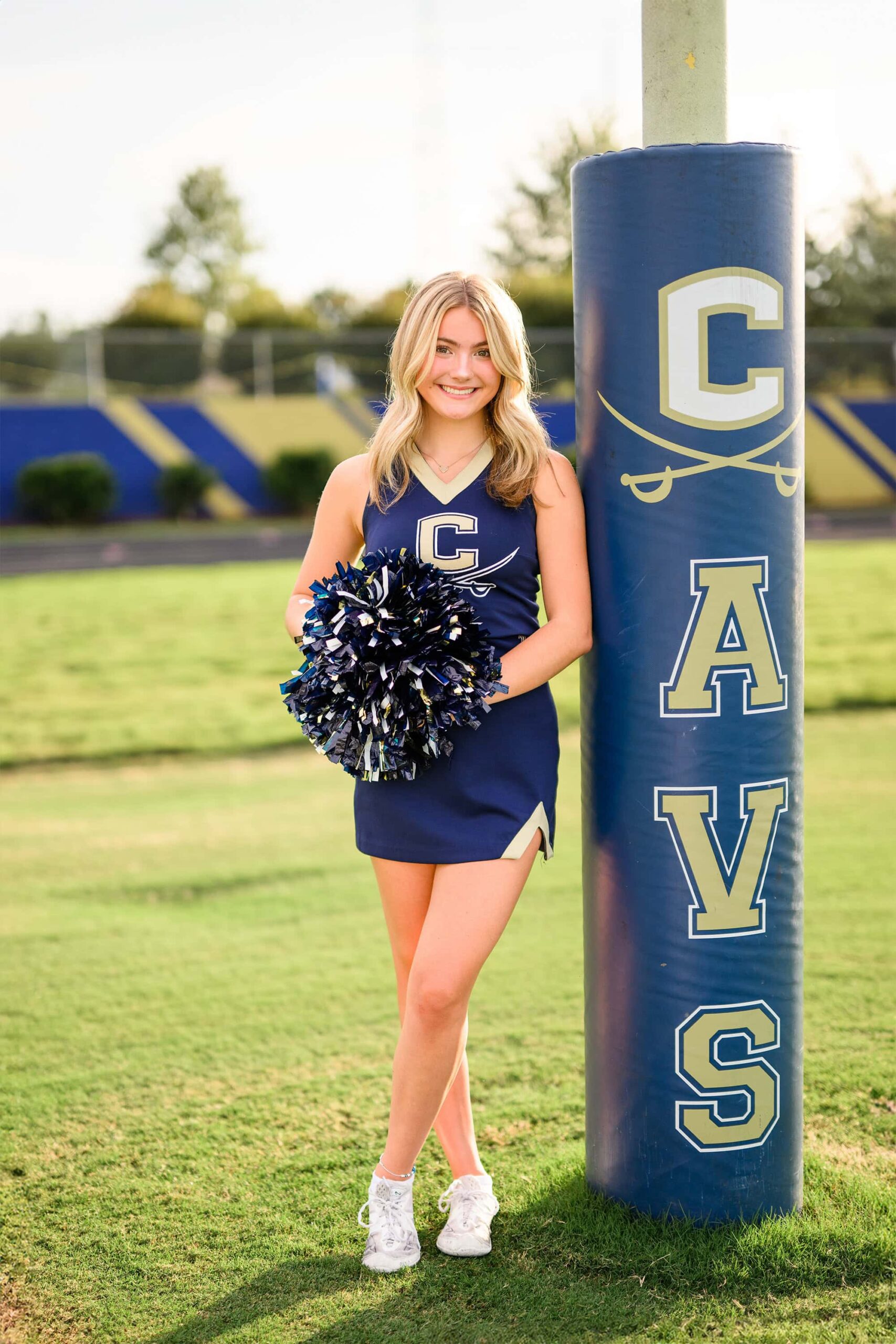 charlotte grad leans against her high school goal post wearing her cheer uniform and holding her poms