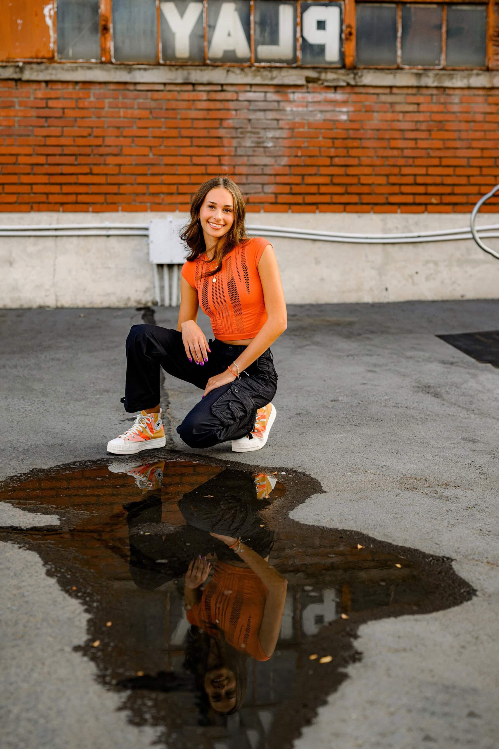 Ardrey Kell grad wears black pants and orange top in senior photo session in camp north end
